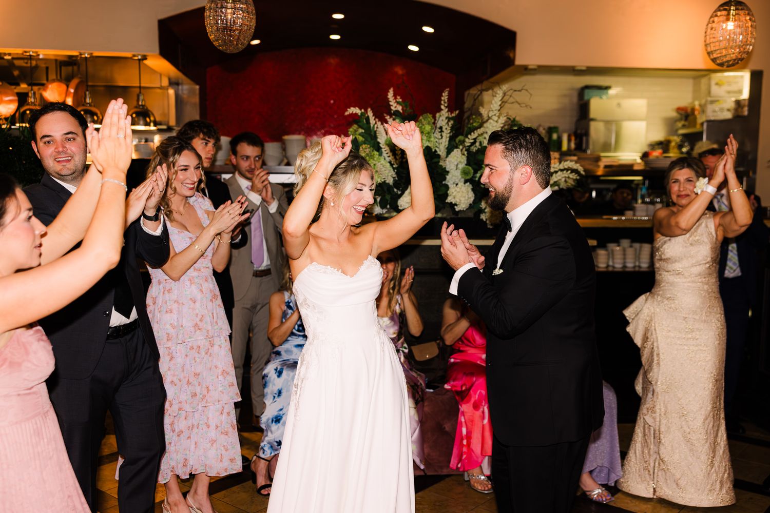 Bride and groom make grand entrance at wedding reception, guests clapping and cheering in elegant venue.