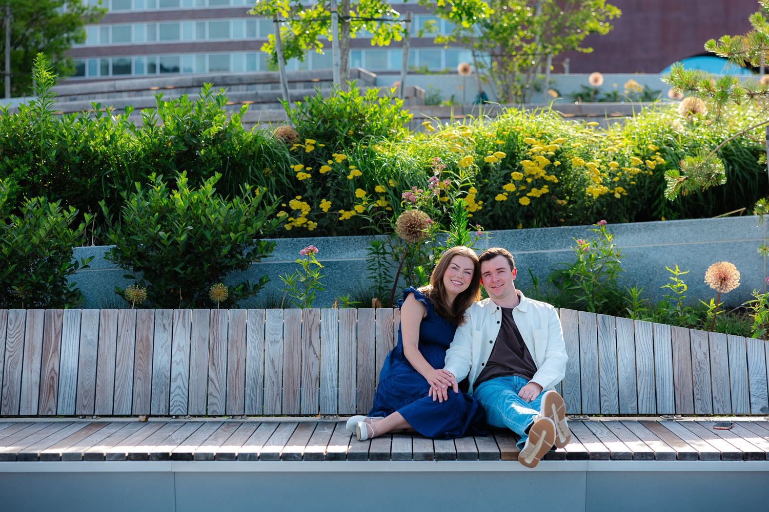 Couple sitting together on wooden bench surrounded by lush green garden plants.