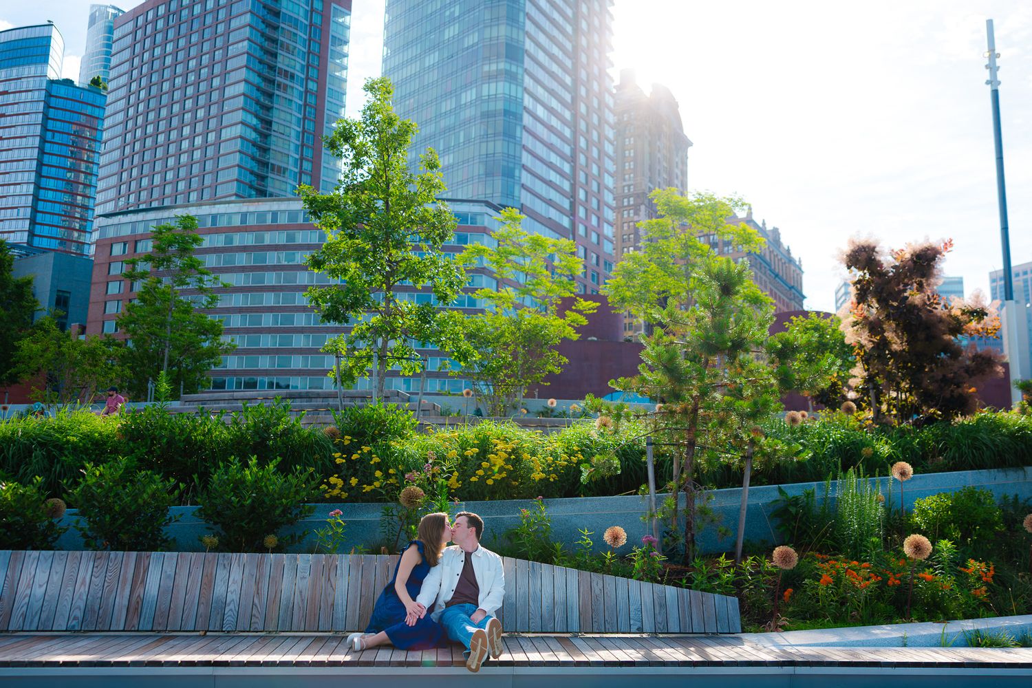 Couple sitting together in a lush urban park with modern skyscrapers and green trees in the background.