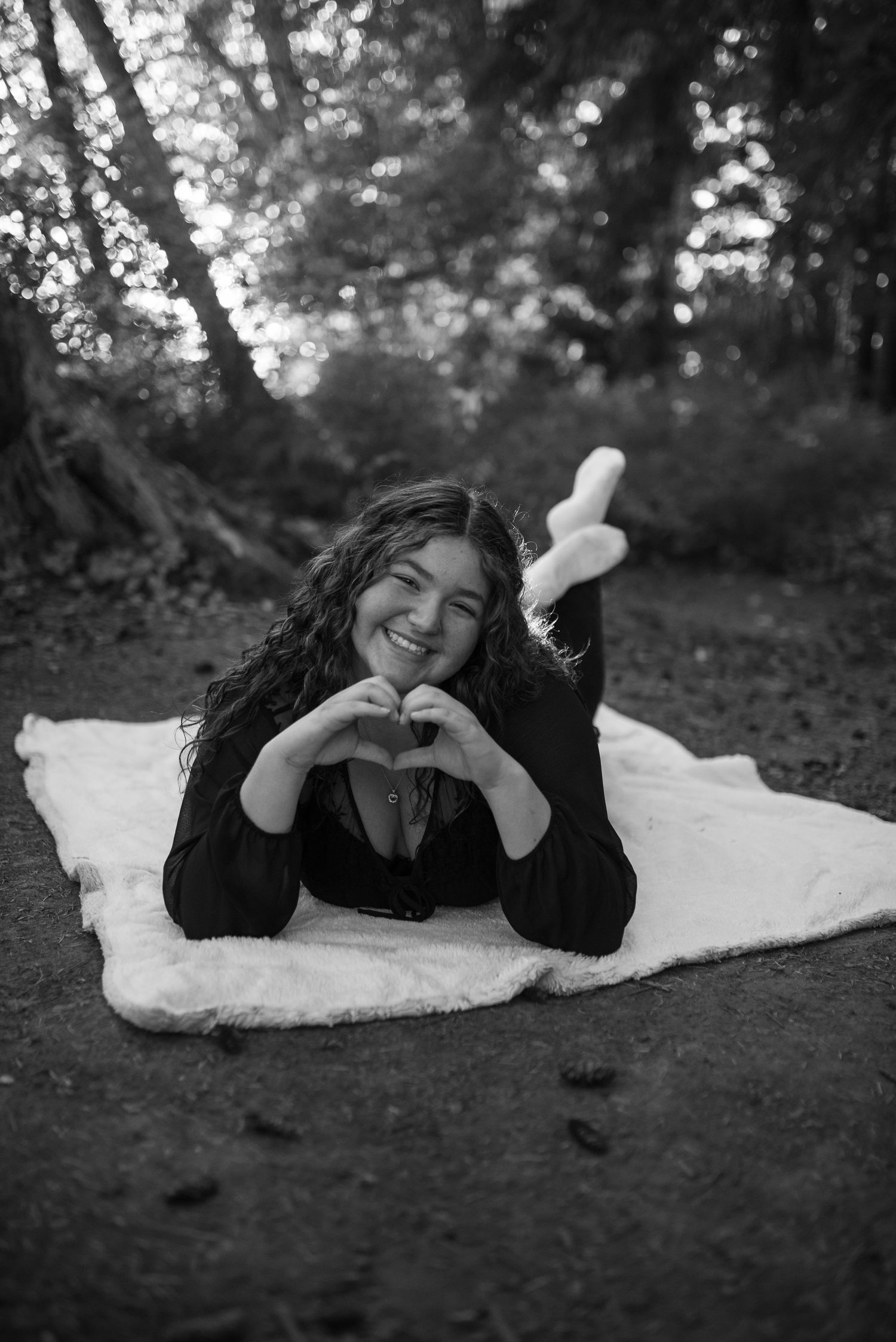 Smiling teen girl makes heart shape with hands lying on blanket outdoors.