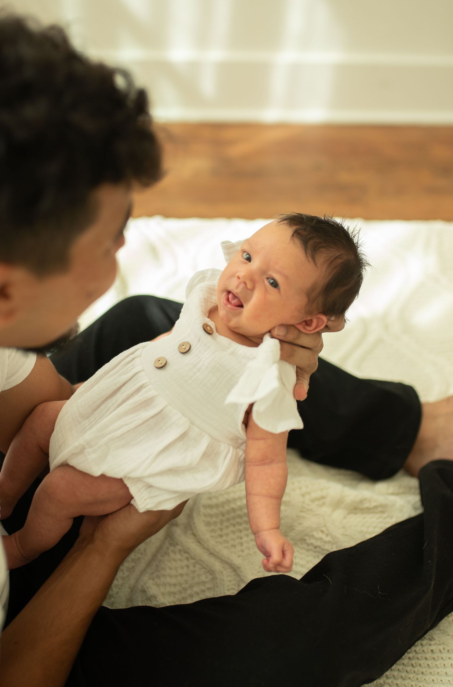 A parent tenderly holds a newborn baby in a white dress, sharing a sweet moment together.