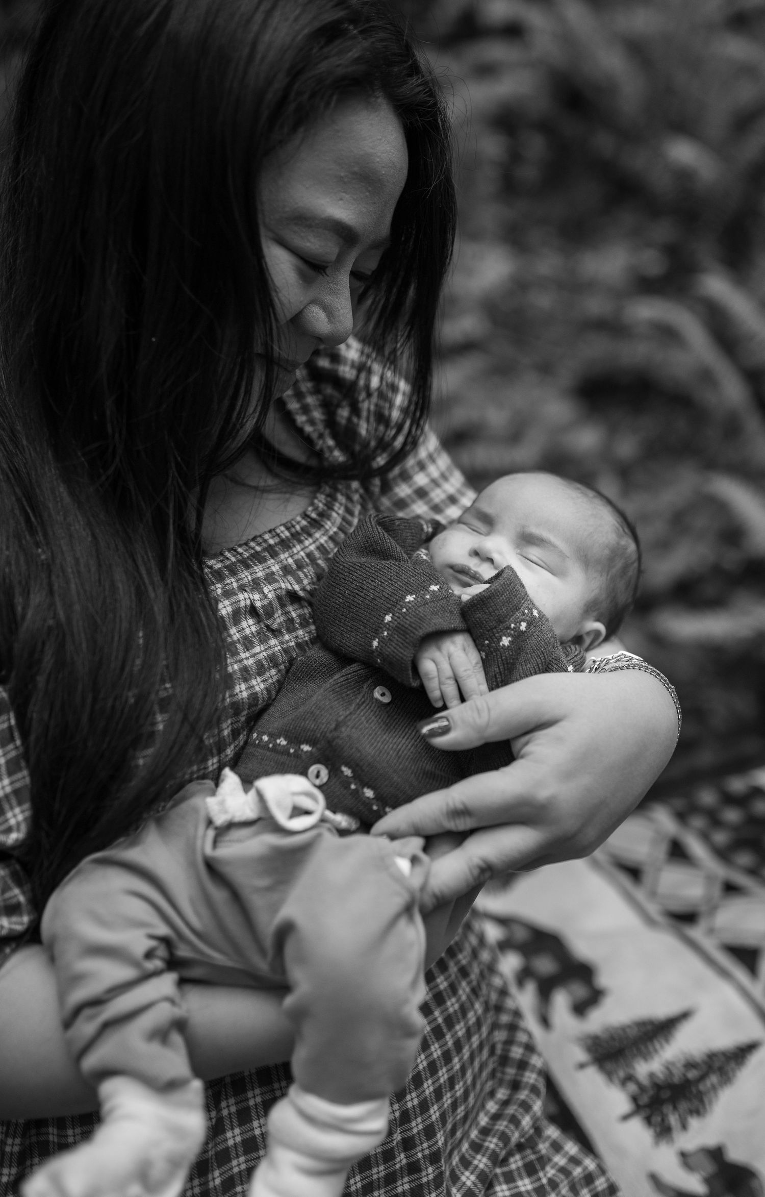 Black and white photo of a mother tenderly cradling her sleeping newborn baby in her arms outdoors.