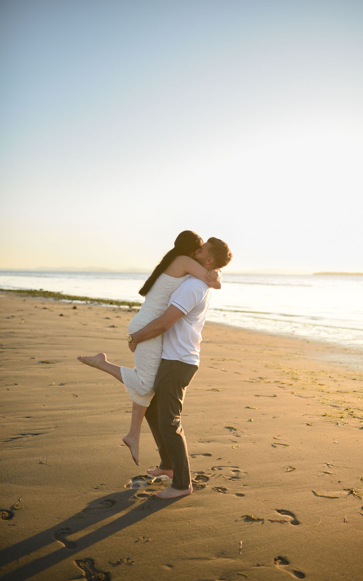 Couple embracing and kissing on a sandy beach at sunset, with ocean waves in the background.
