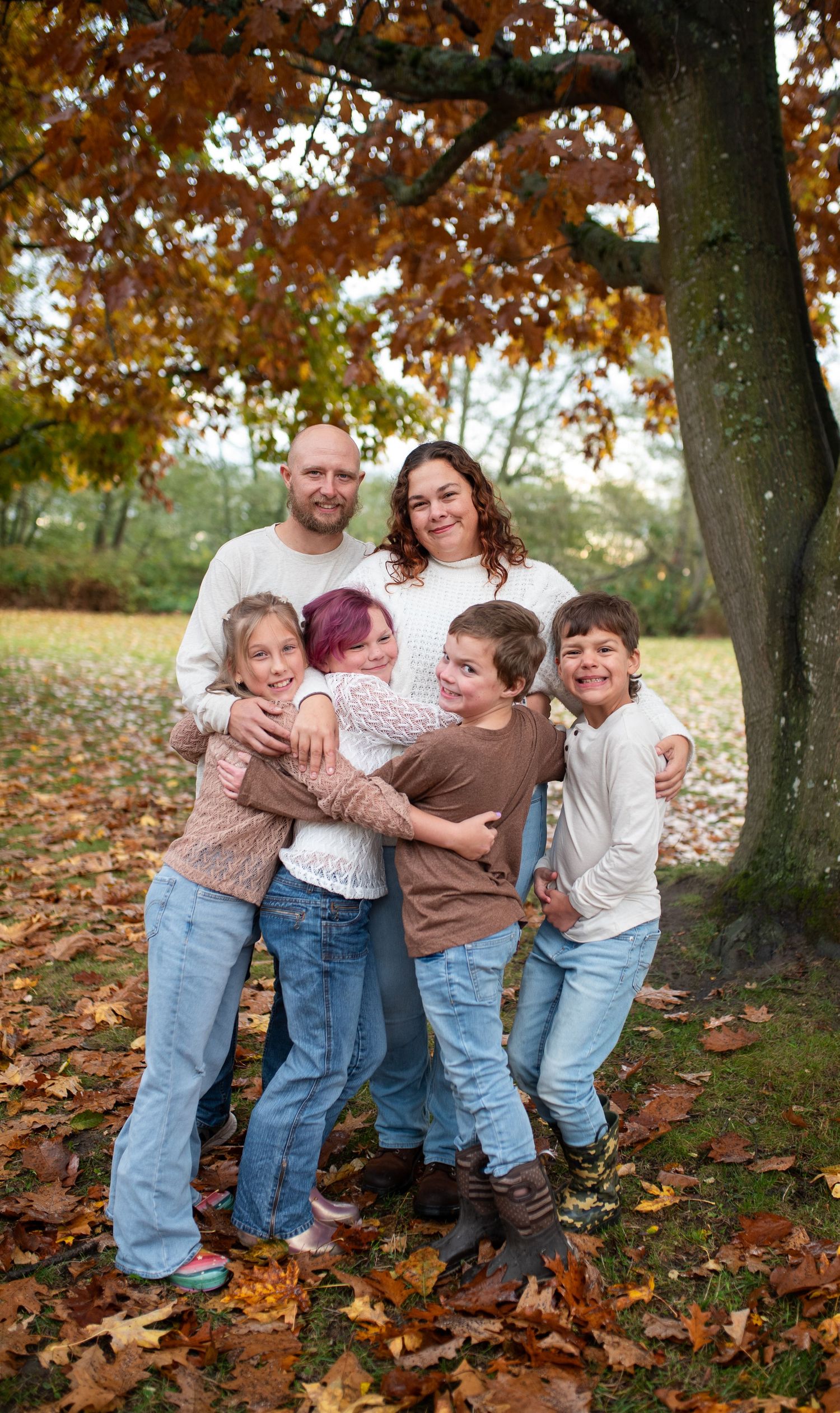Happy family of six posing together under colorful autumn foliage in a park.