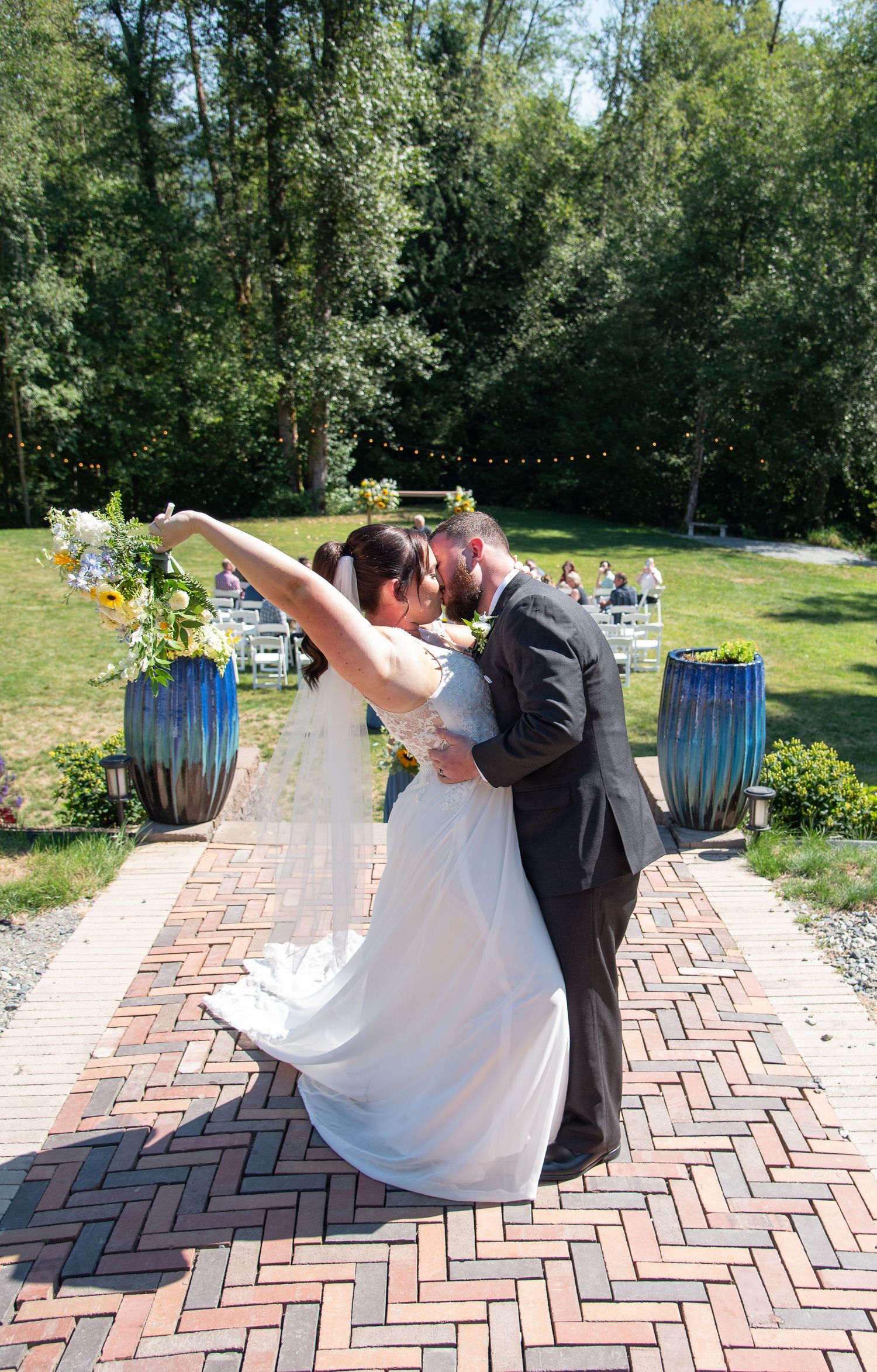 A newlywed couple shares a romantic dip kiss on a herringbone brick patio after their ceremony.