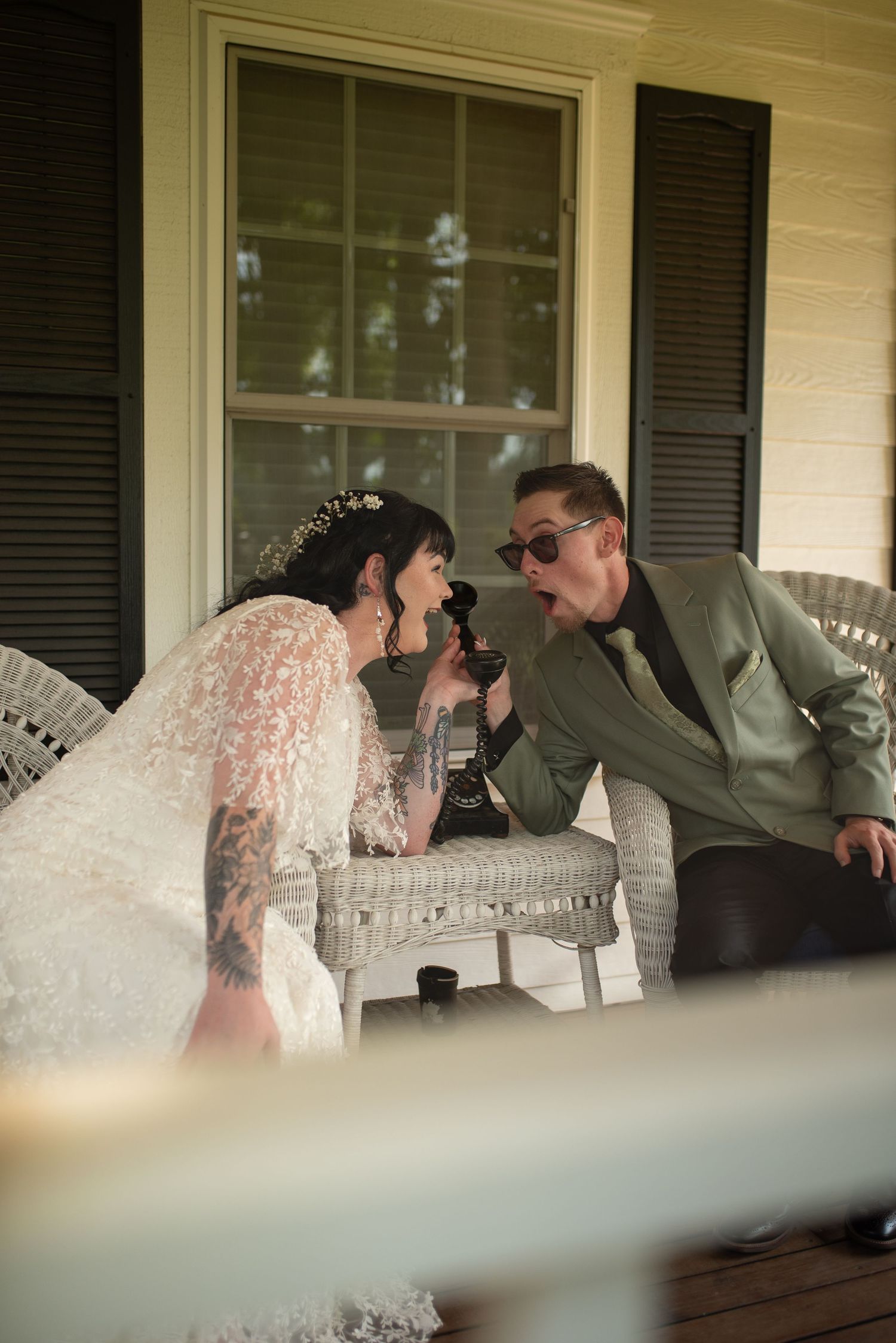 Bride and groom sharing a fun moment on a porch, laughing together over a bottle at their wedding.