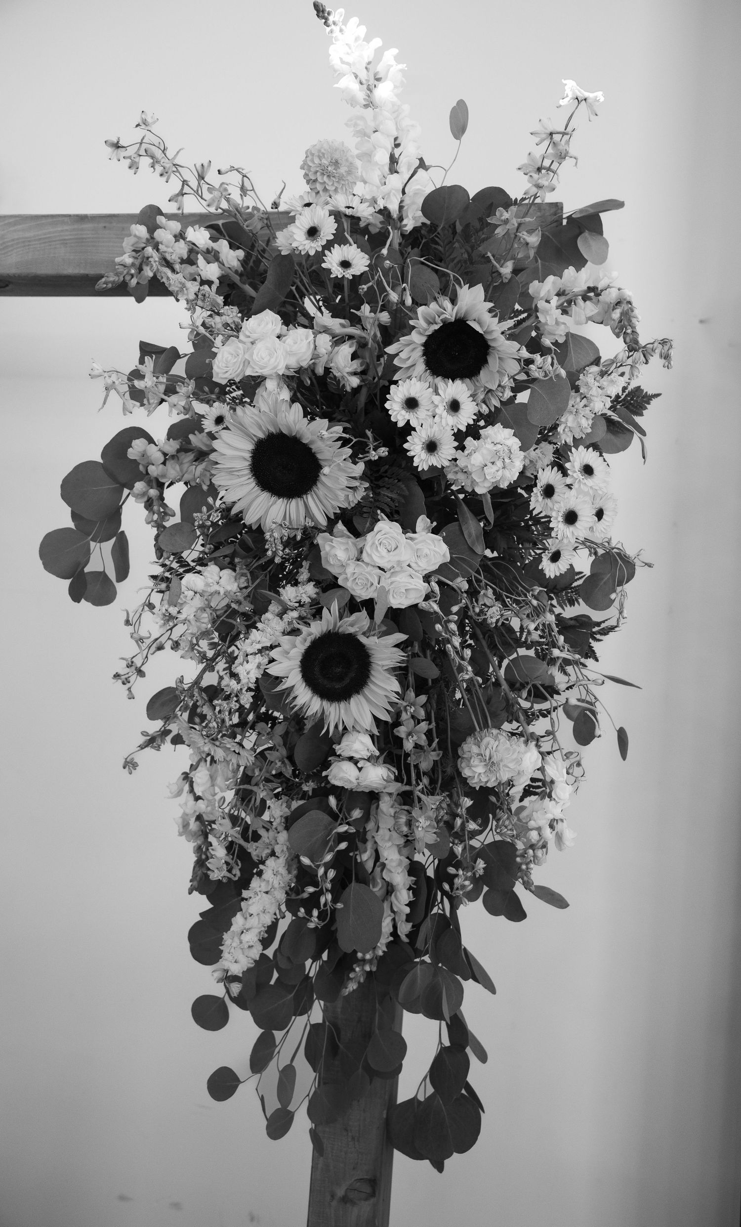 Black and white photo of a cascading wedding floral arrangement featuring sunflowers and mixed blooms on a wooden stand.