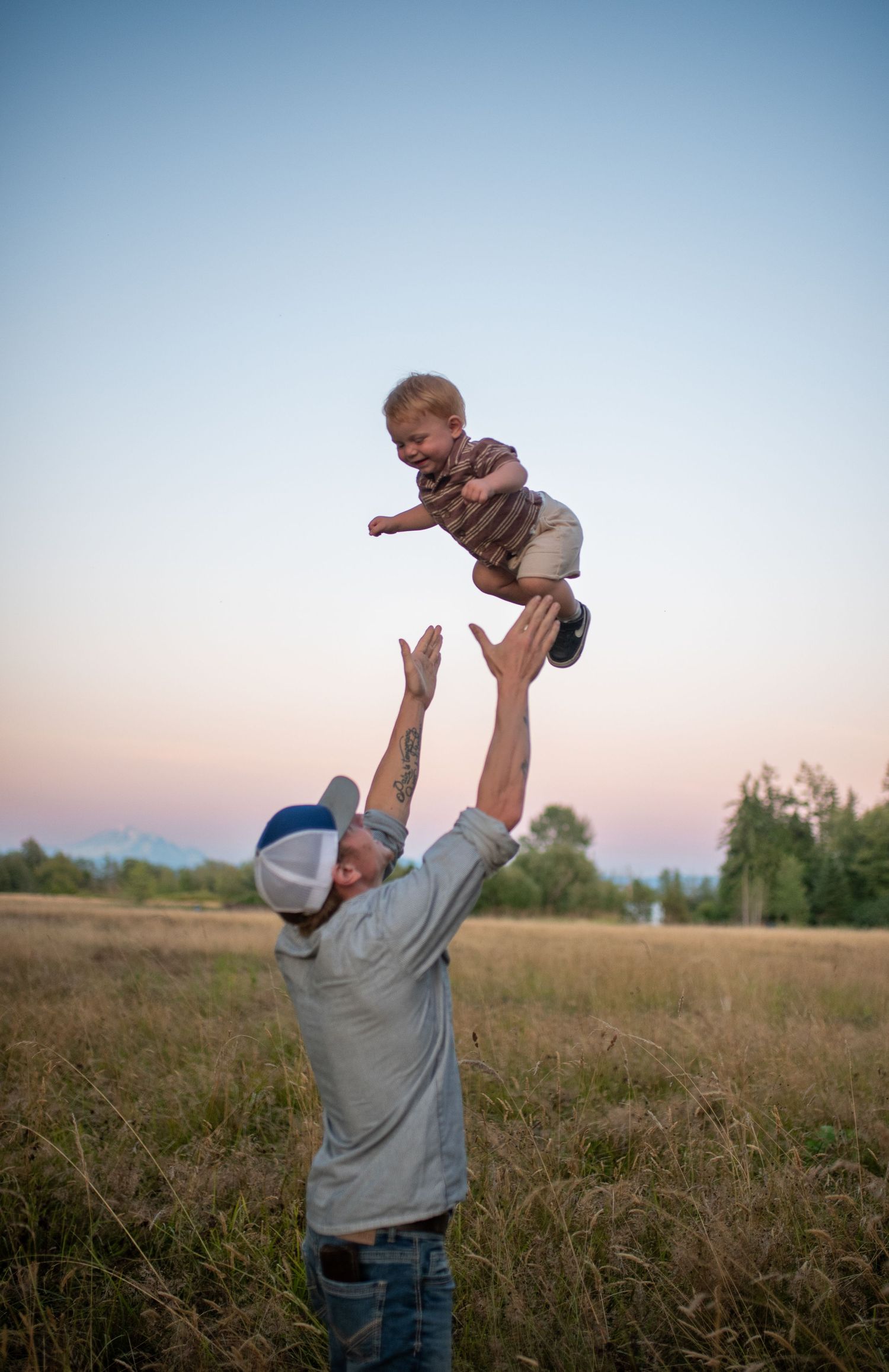 Father joyfully tosses smiling baby in the air in a golden field at dusk.