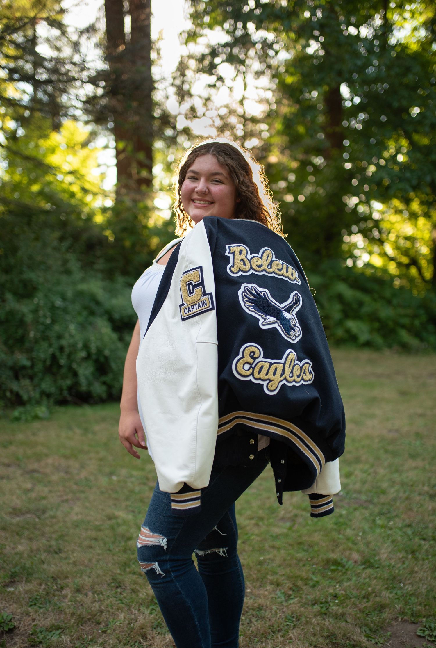 Teen girl smiles wearing Belew Eagles varsity letterman jacket outdoors.
