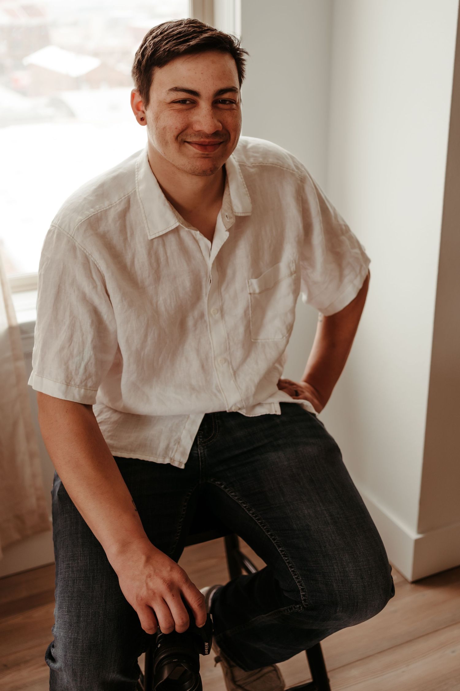 Smiling young man in a white linen shirt sitting casually in a bright room.