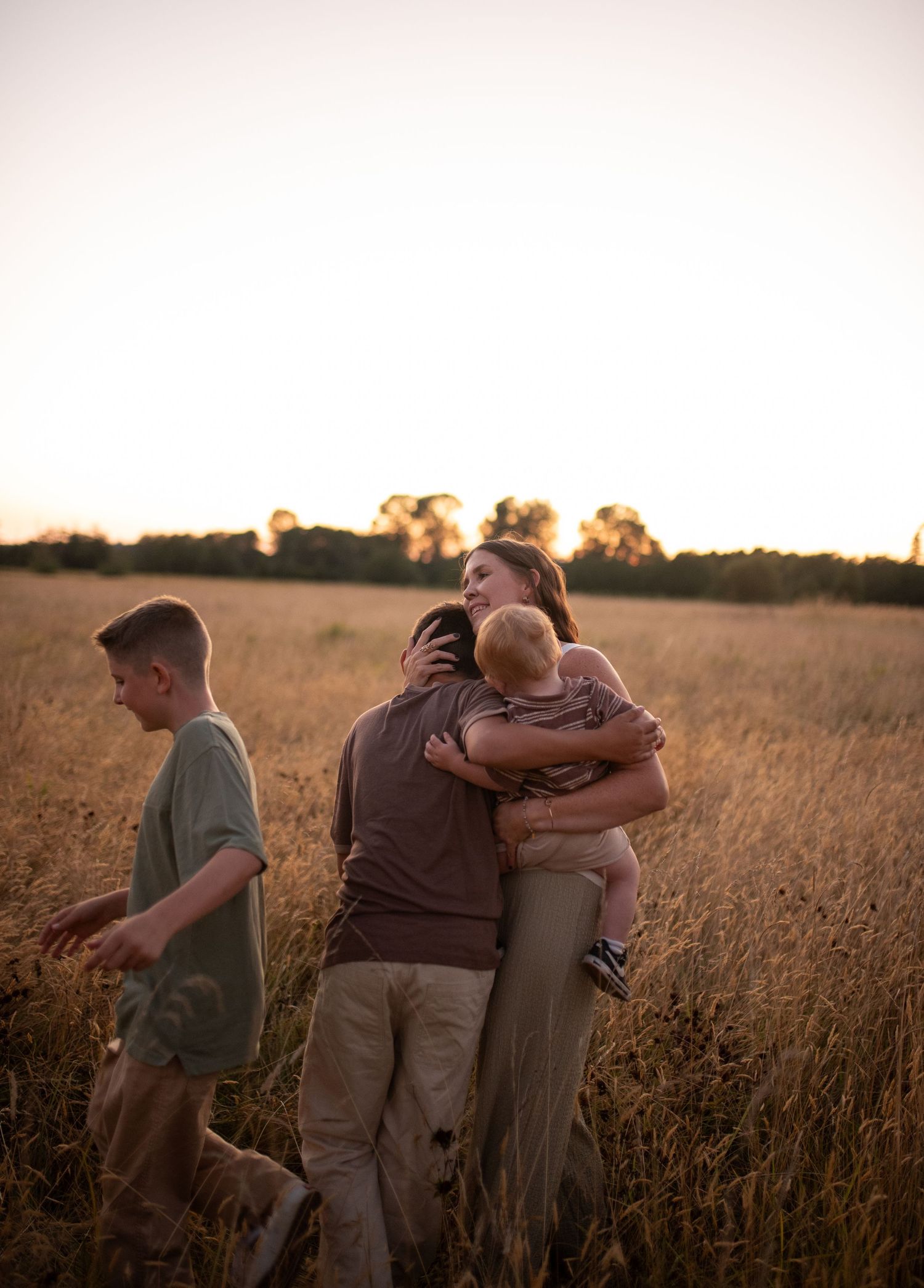 Family sharing a warm embrace in a golden wheat field during a beautiful sunset.
