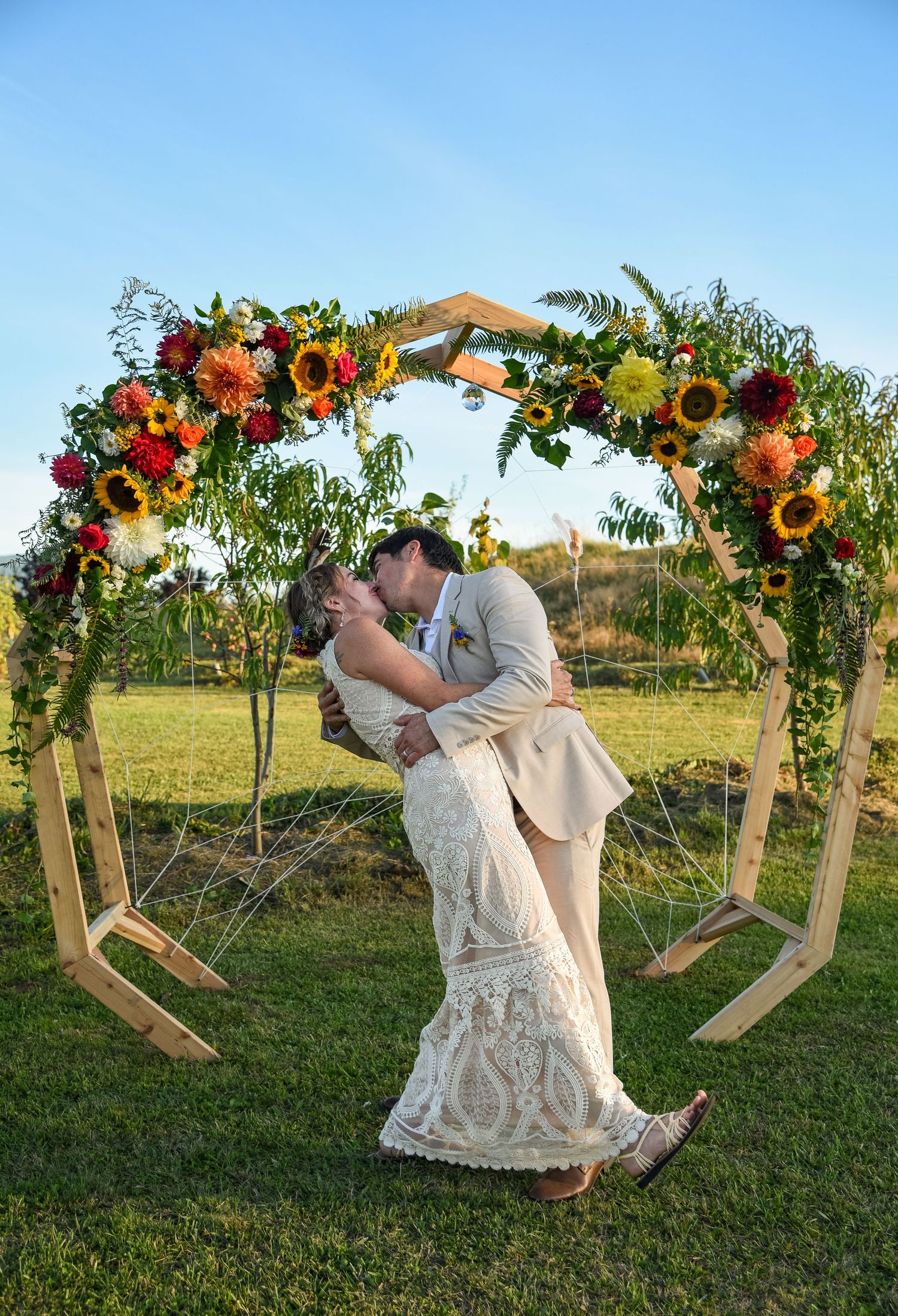 Bride and groom sharing a dip kiss under a floral arch with sunflowers at golden hour.