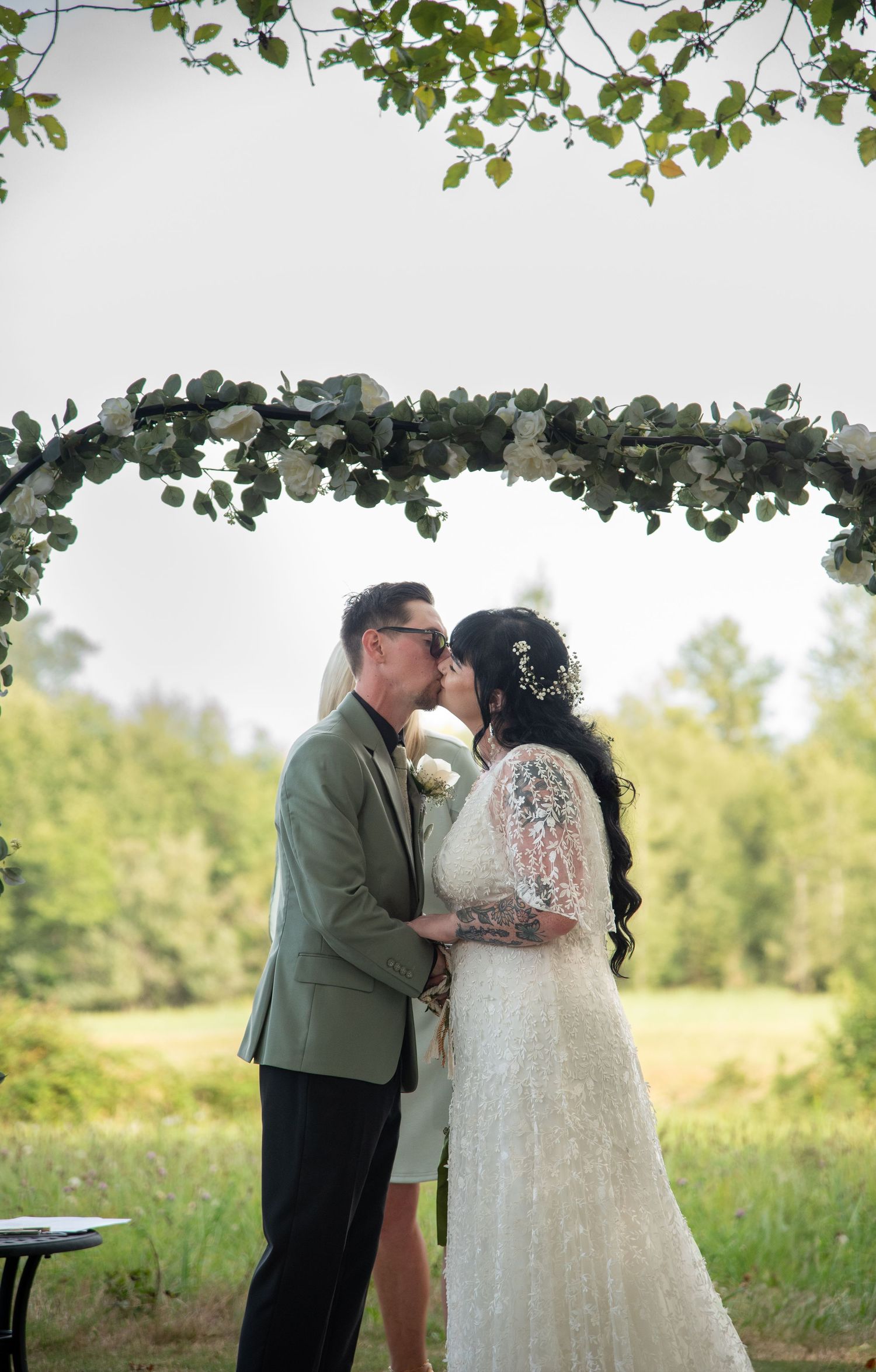 Bride and groom share first kiss under floral arch with eucalyptus greenery at outdoor wedding ceremony.
