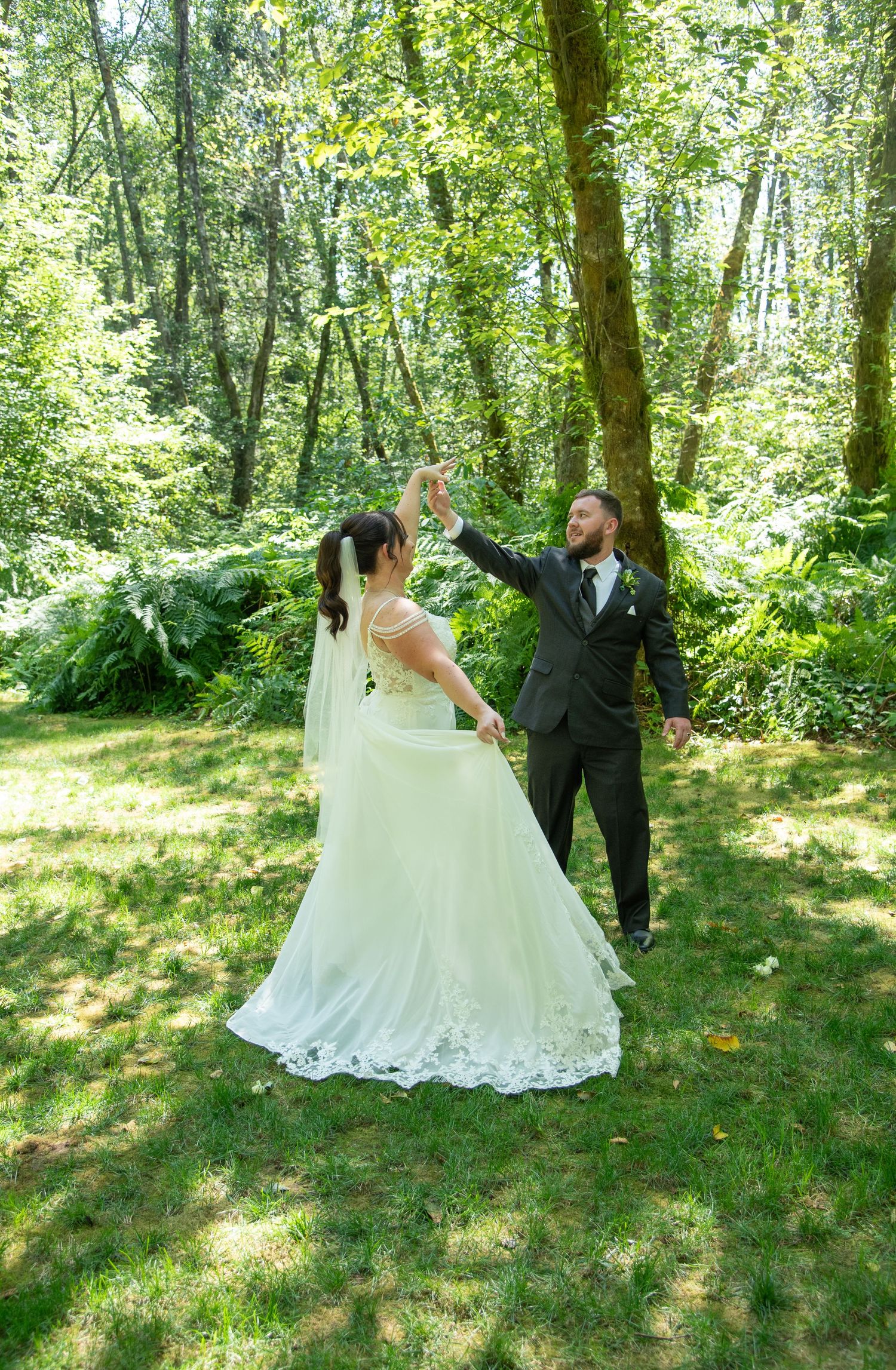Bride and groom dancing outdoors in a lush green forest setting, with the groom spinning his bride in her white wedding gown.