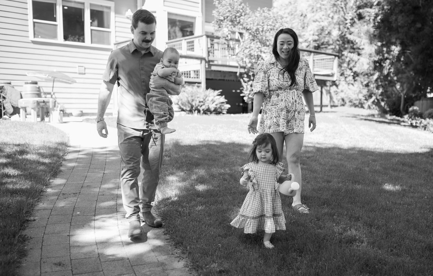 Young family walking together on garden path in black and white photo.
