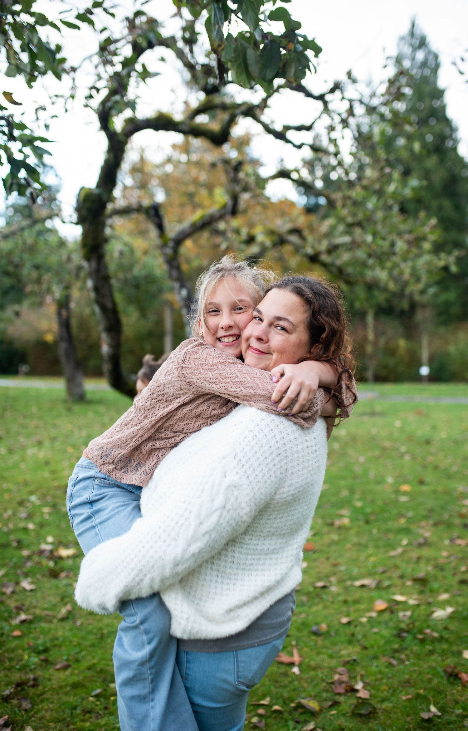 Mother hugs daughter outdoors in a green park during autumn.