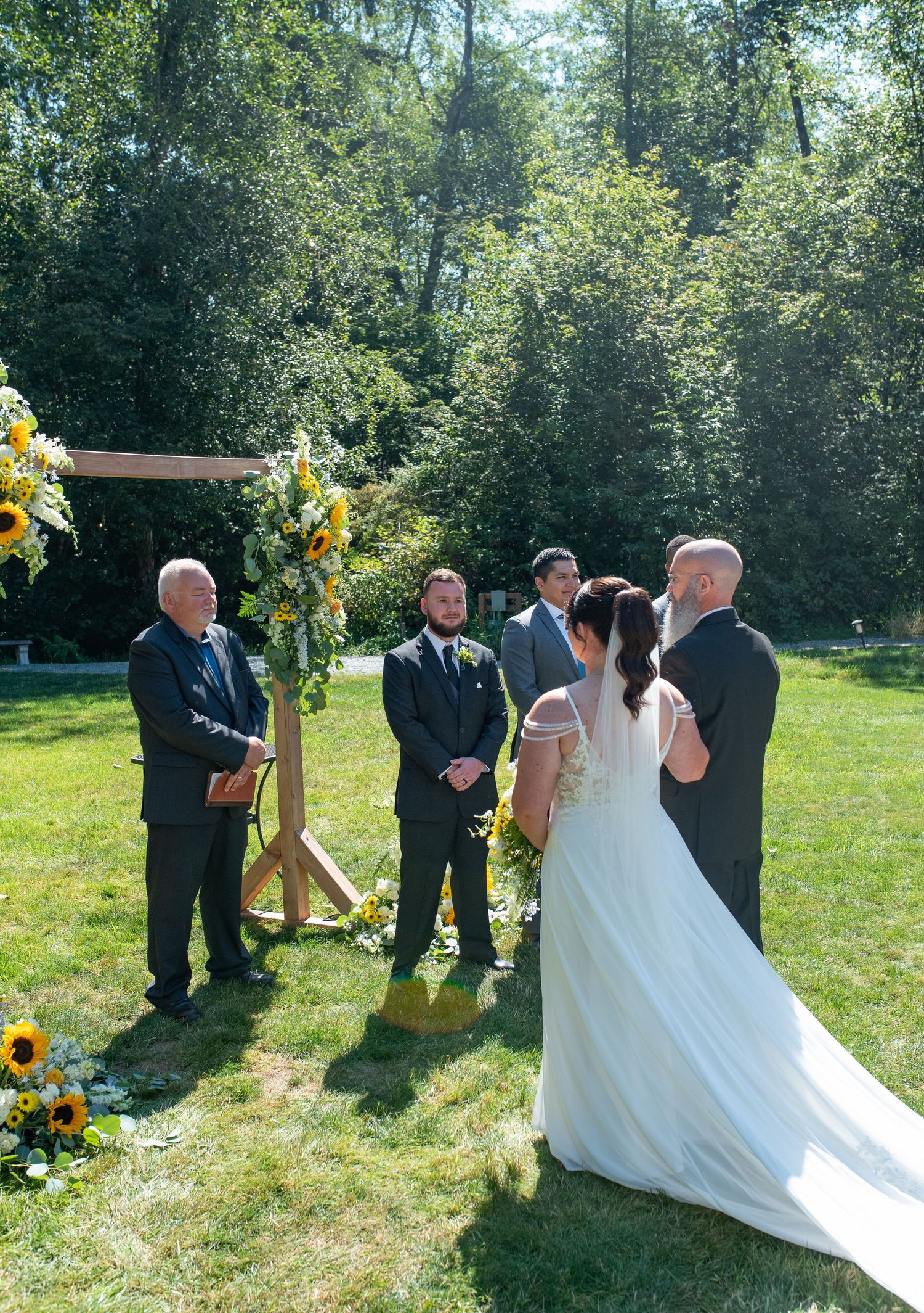 A bride and groom exchange vows at an outdoor sunflower-decorated wedding ceremony altar.