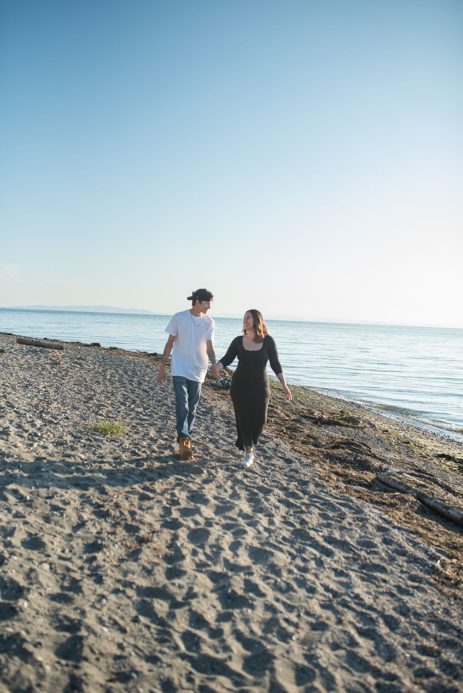 A couple walks hand in hand along a sandy beach on a bright clear day.