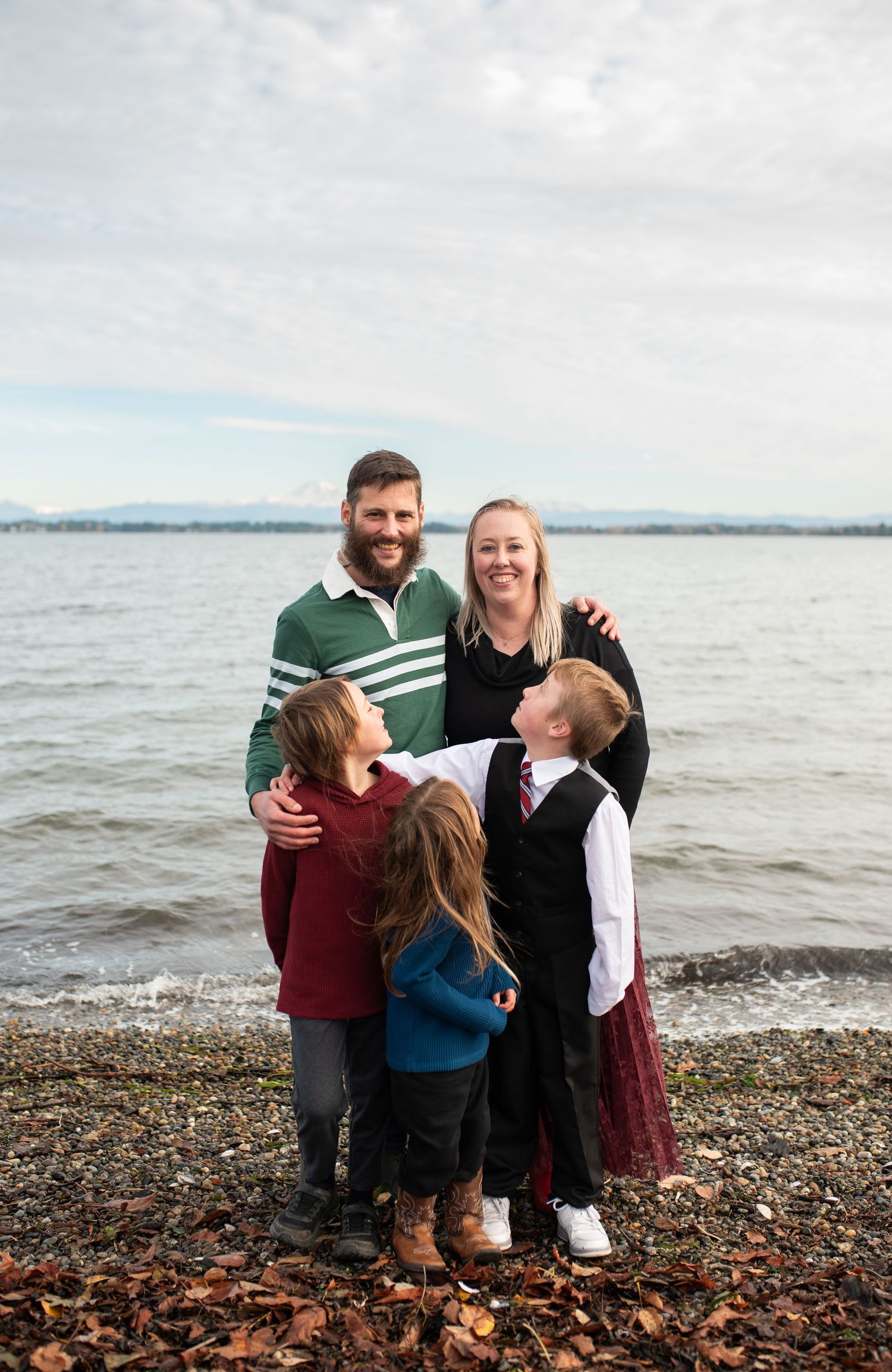 Happy family of five posing together on rocky beach shoreline on cloudy day.