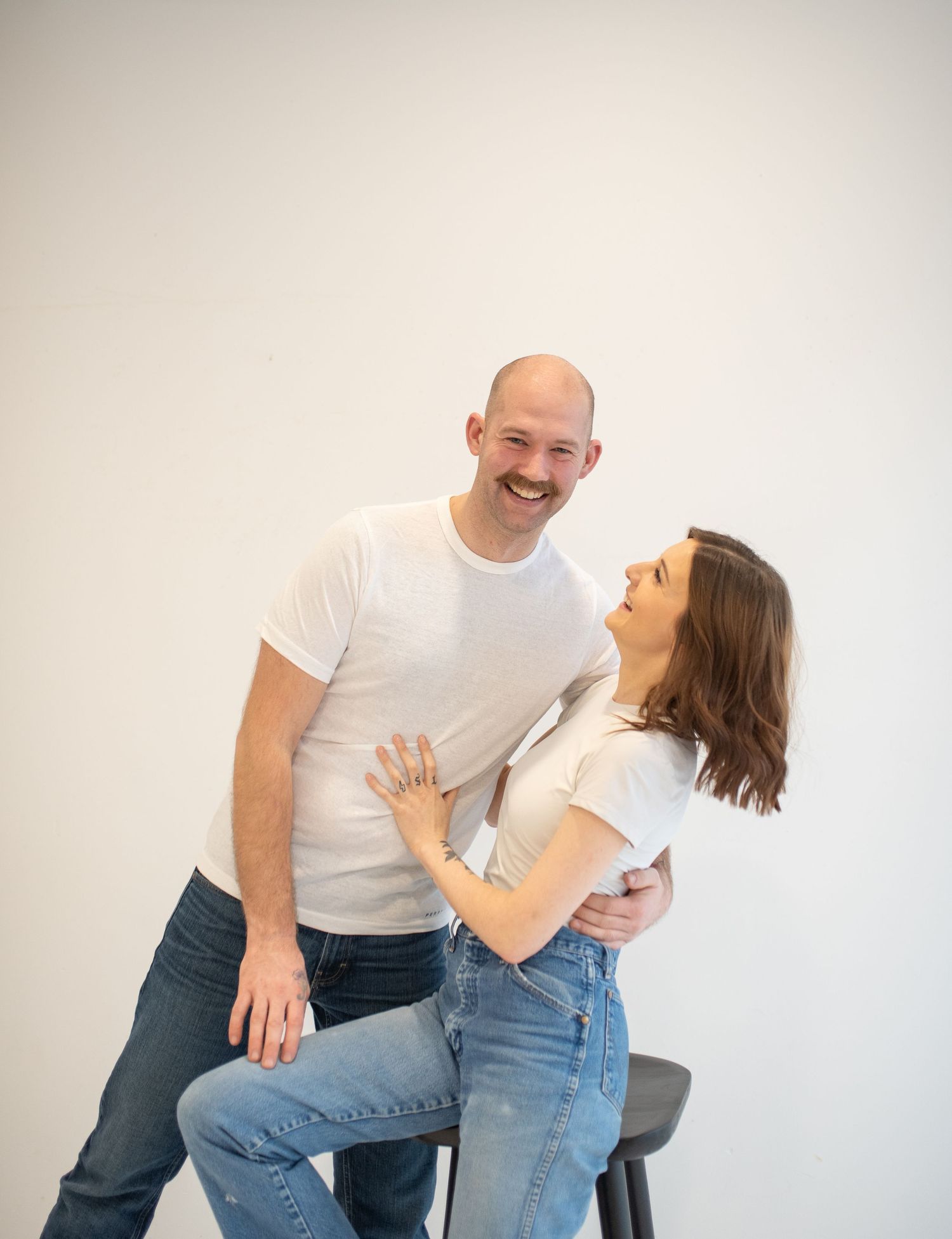 Laughing couple in matching white tees and jeans sharing a joyful moment during an engagement photo session.