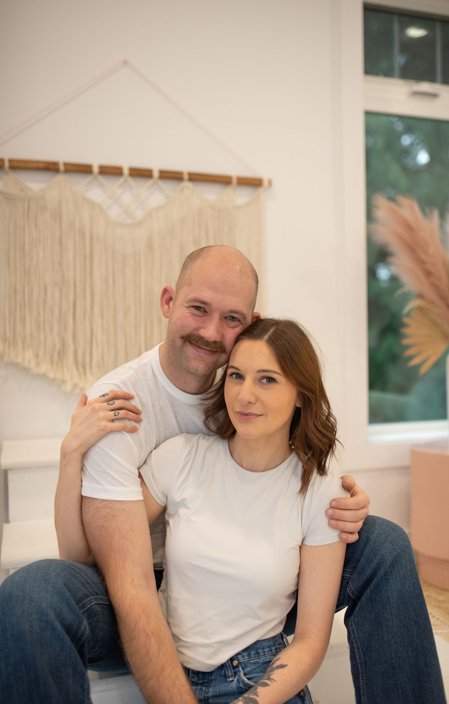 Couple in matching white t-shirts and jeans posing together in a bright boho-styled photography studio.
