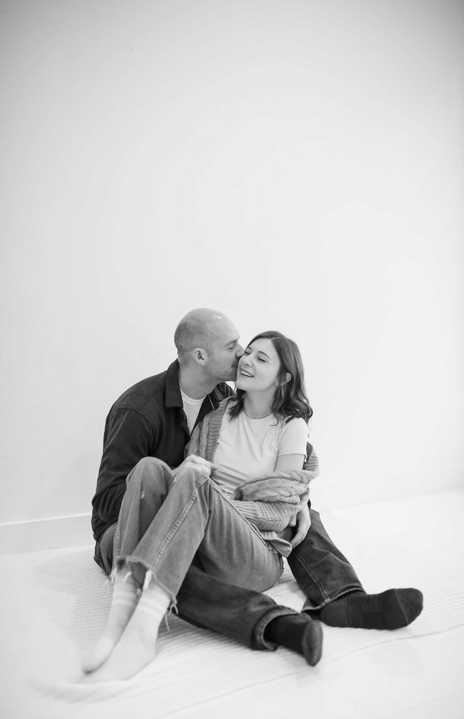Black and white photo of couple sitting on floor sharing a kiss during an engagement session.