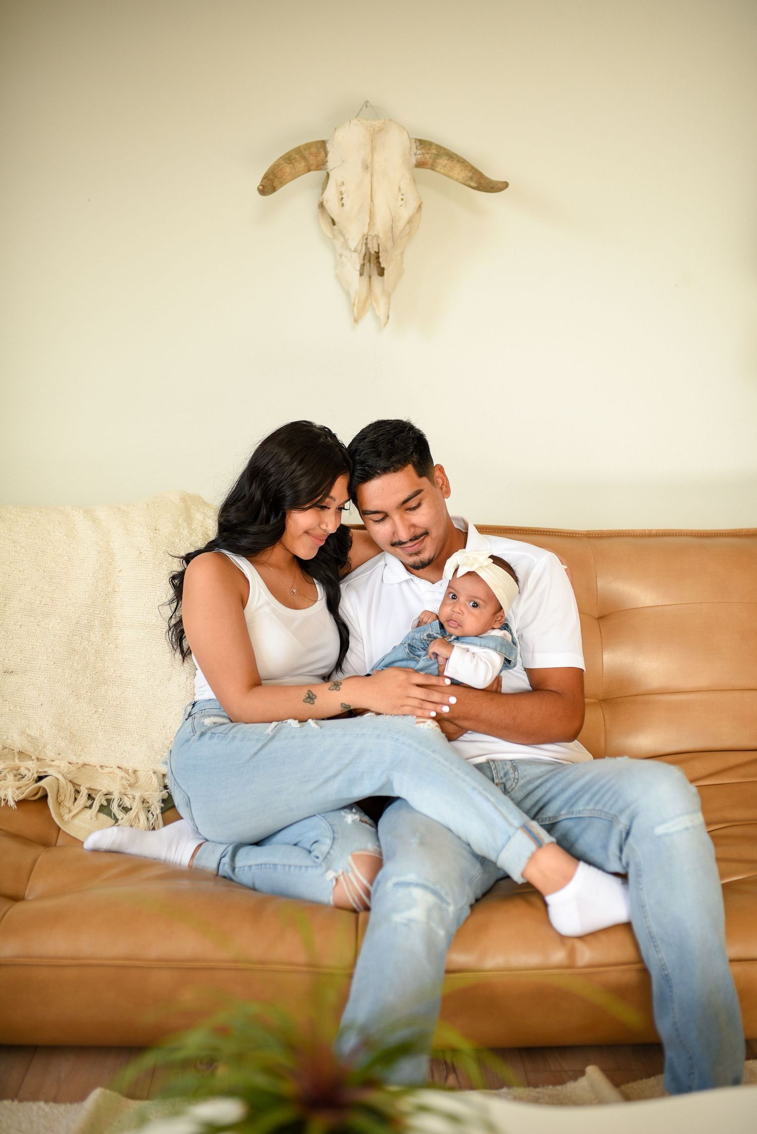 Young couple sitting on leather sofa admiring their newborn baby in a cozy home setting.