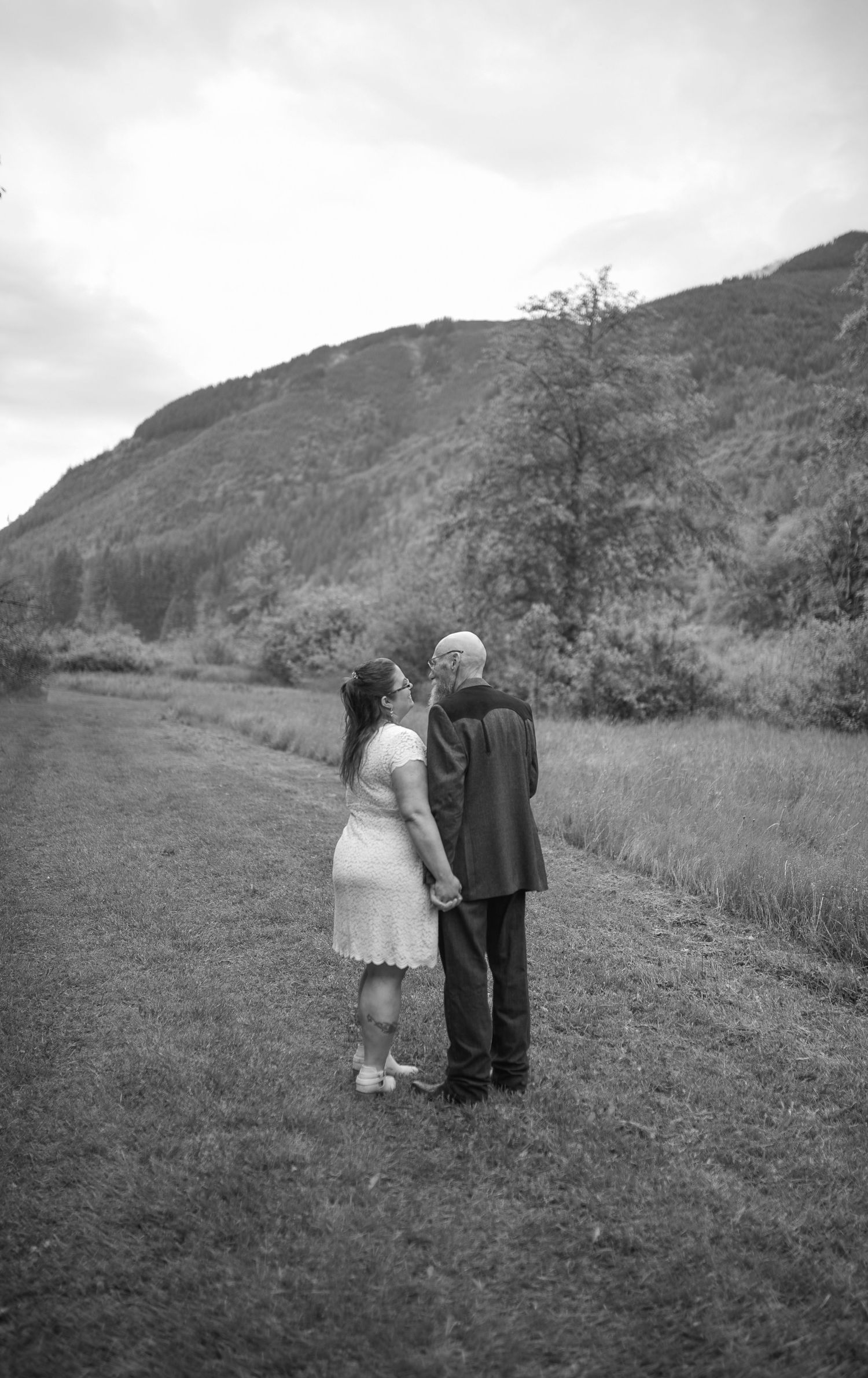 Black and white photo of a couple kissing in a meadow with a mountain backdrop on their wedding day.