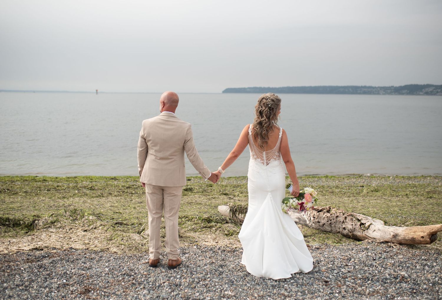 Bride and groom hold hands while gazing at scenic ocean view on their wedding day at waterfront venue.