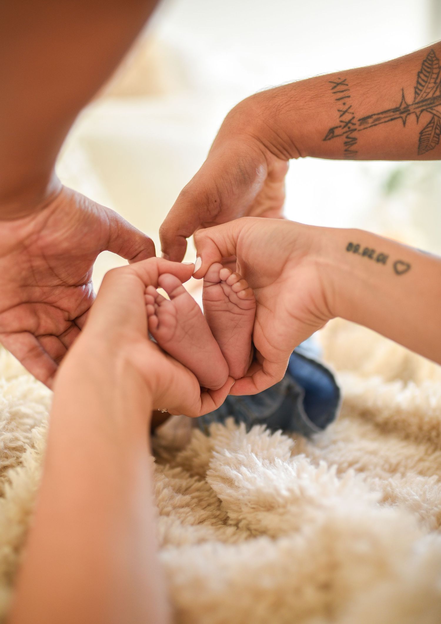 Two adults cradling a newborn baby's tiny feet in their hands on a soft fluffy white blanket.