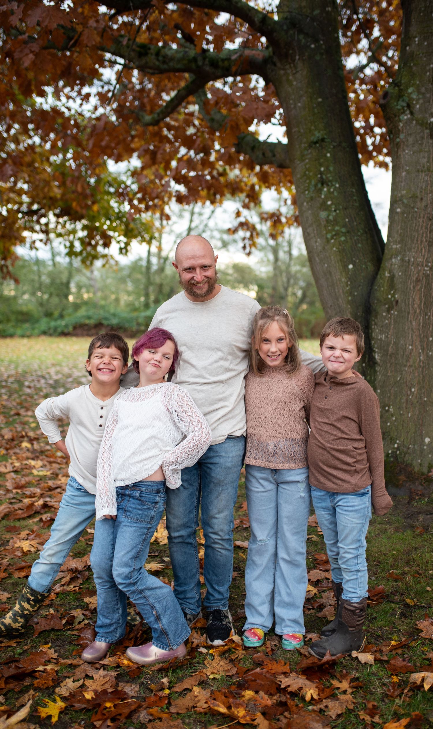 Father poses with four children among autumn leaves in a park.