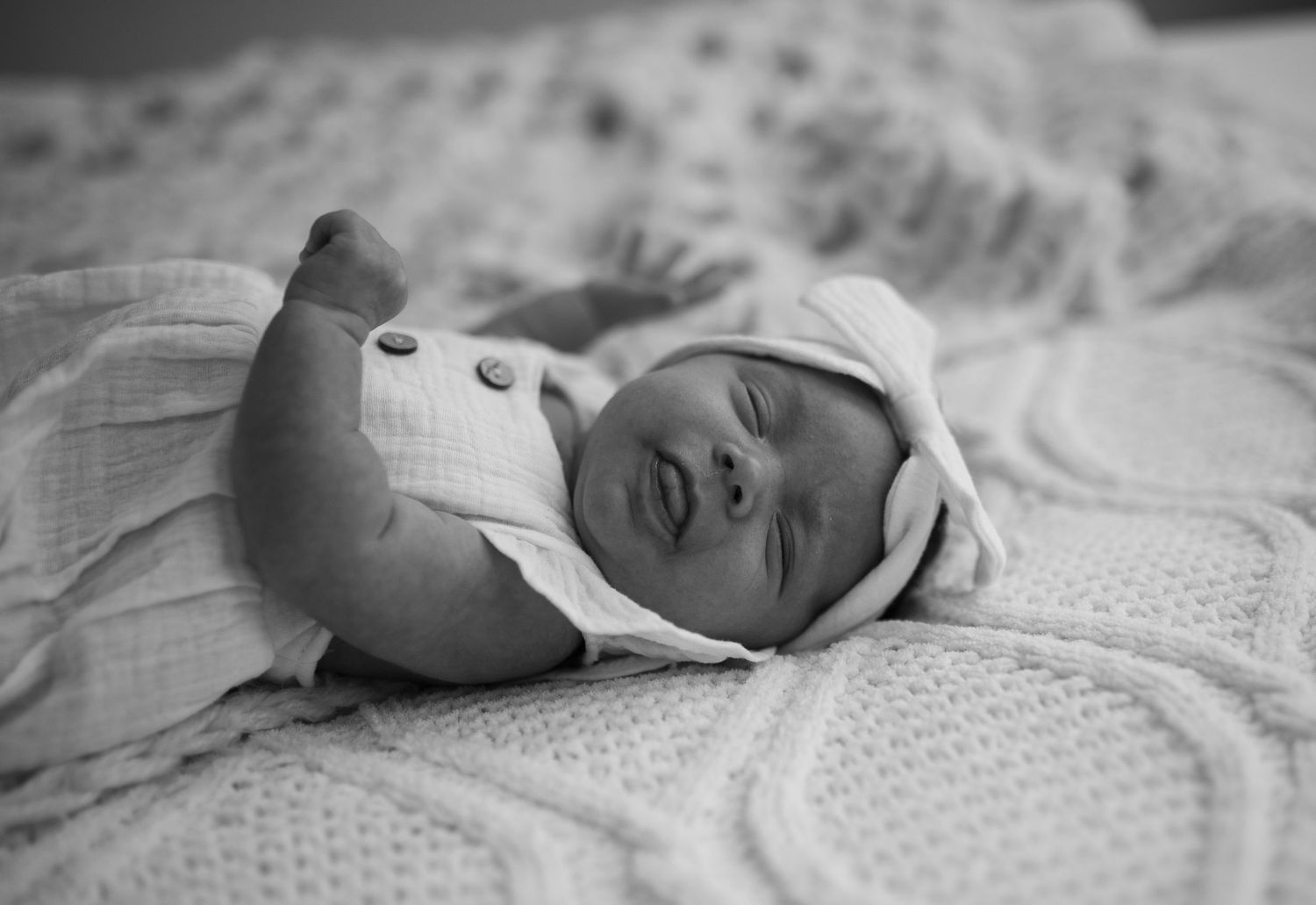 Black and white portrait of a peaceful newborn baby swaddled in white on a knit blanket.