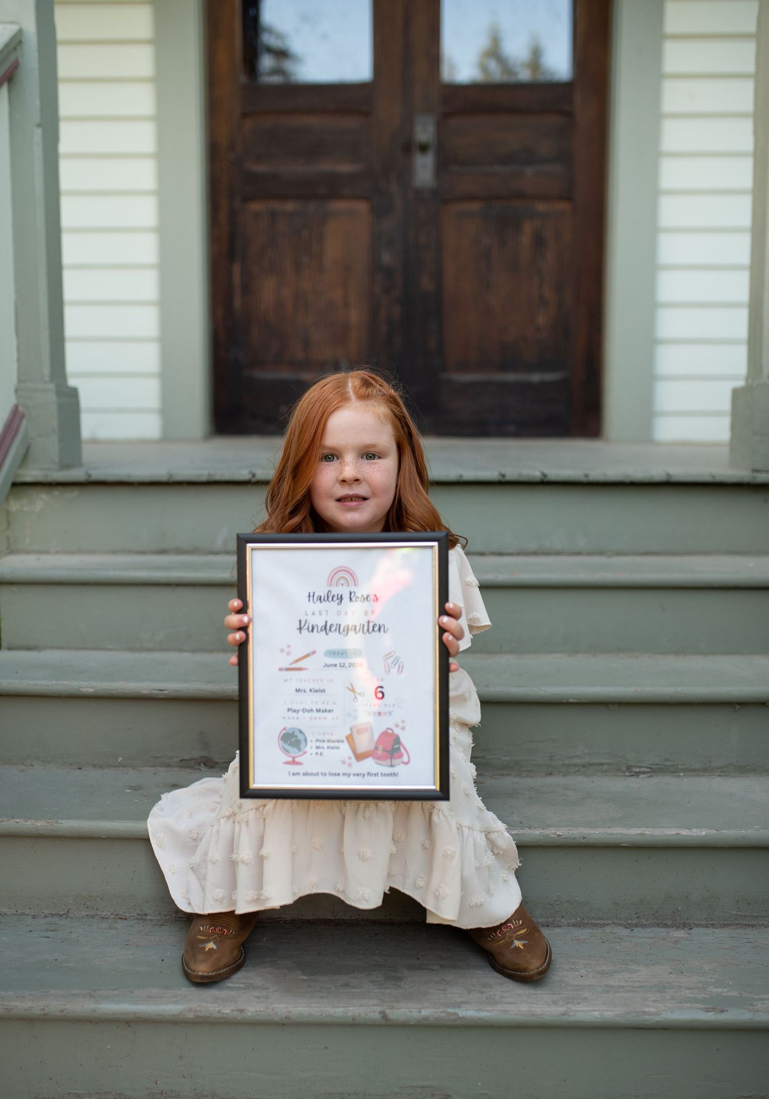 Red-haired girl holding kindergarten certificate on vintage building steps.