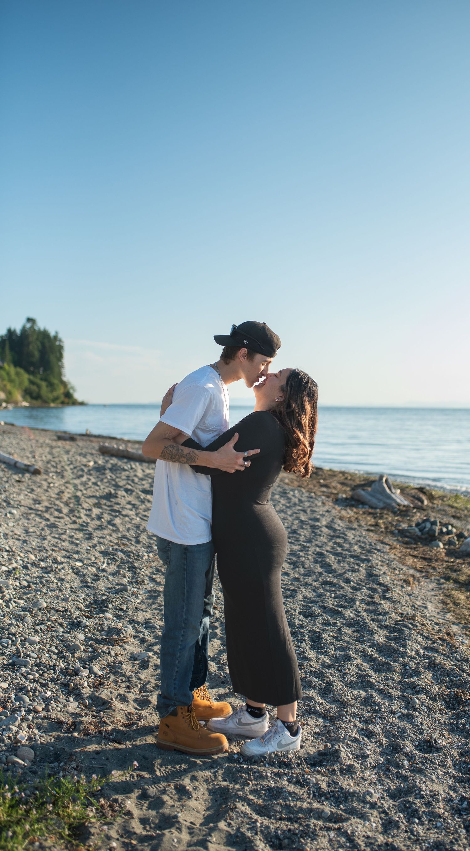 A young couple shares a kiss on a pebble beach on a clear sunny day.