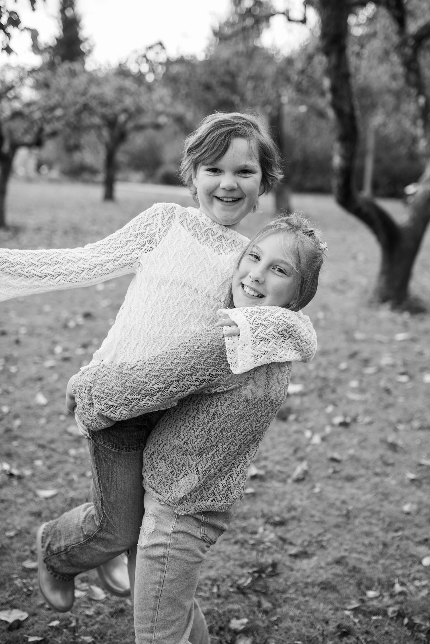 Two girls laughing as one gives the other a piggyback ride in an autumn park.