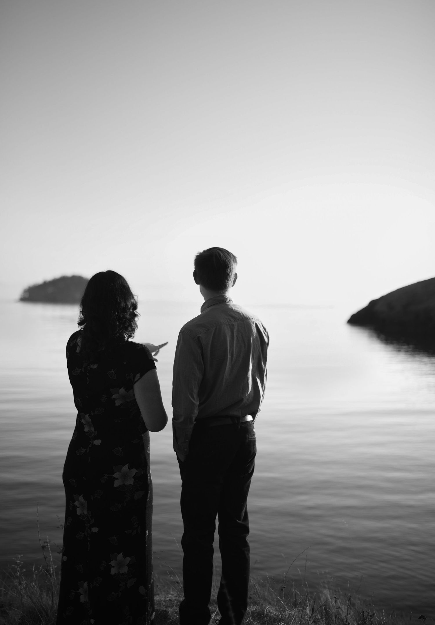Black and white silhouette of couple standing together overlooking a calm ocean with islands.