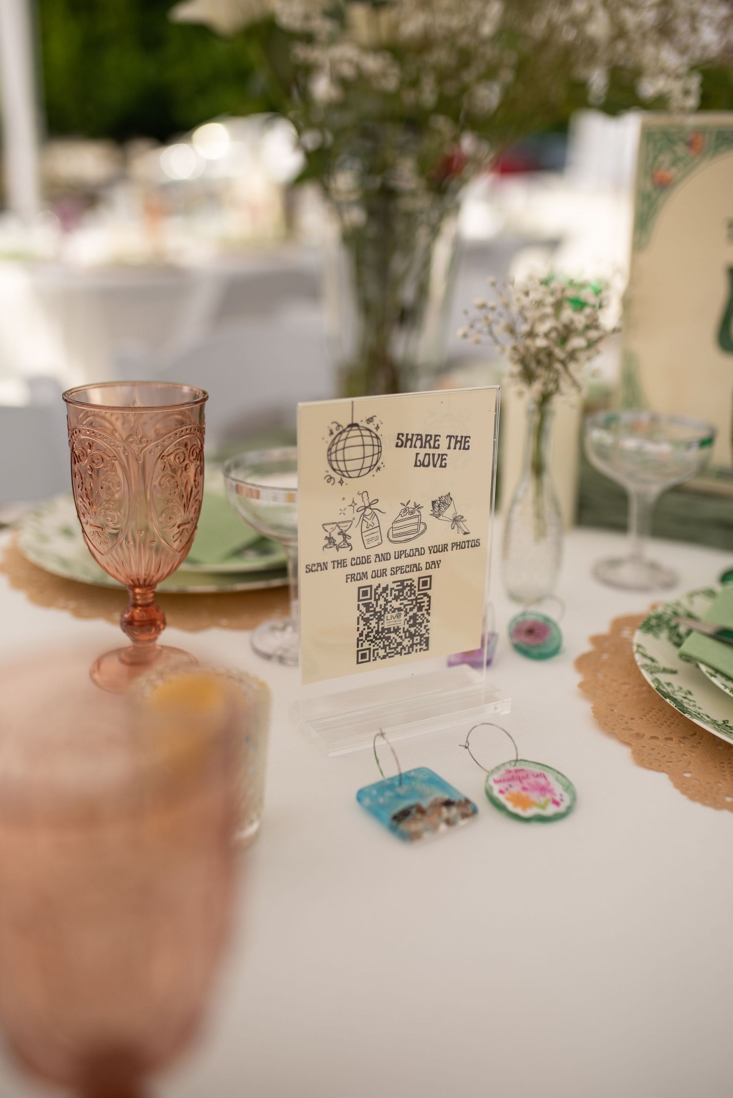 Elegant wedding table setting with pink glassware, QR code share sign, and floral centerpieces.