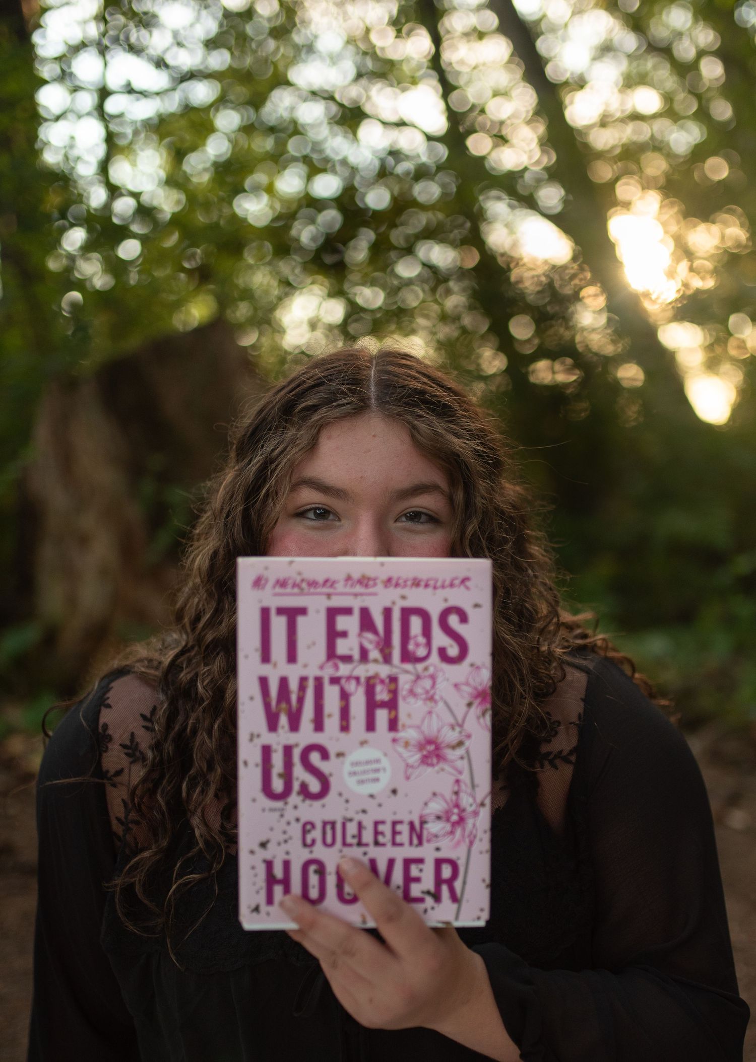Teen girl holds Colleen Hoover book It Ends With Us in forest.