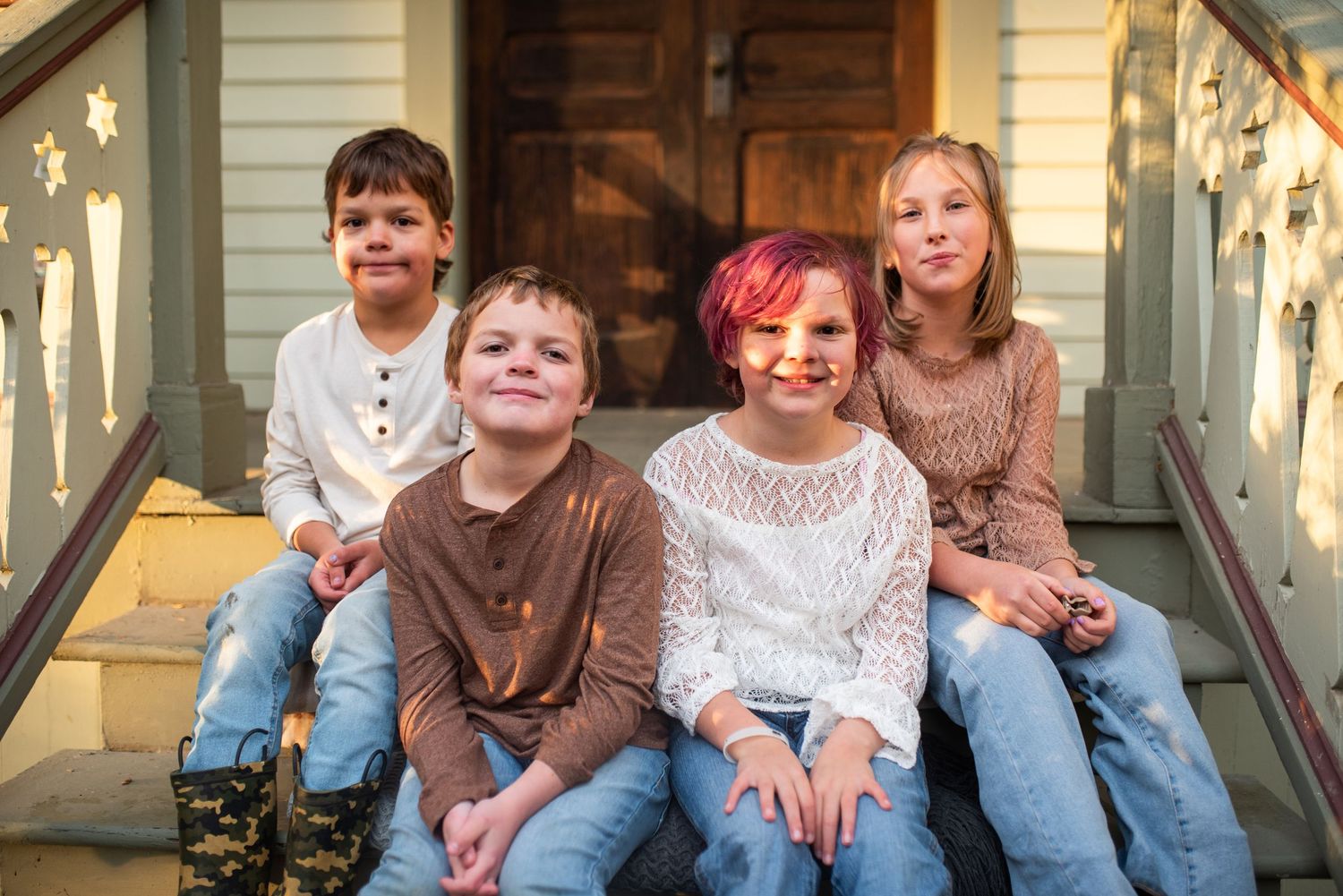 Four children sitting together on front porch steps smiling for a family portrait.
