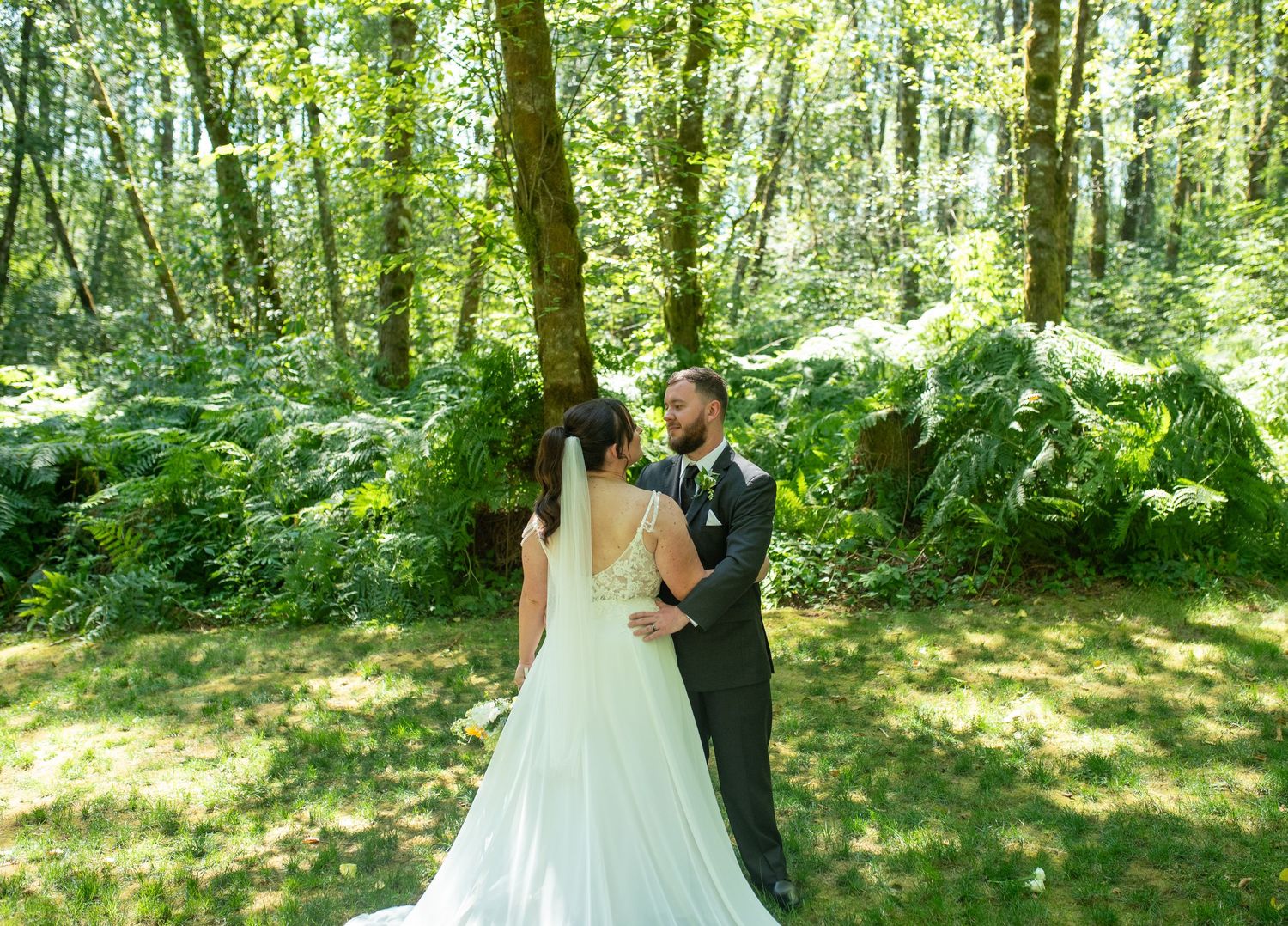 A bride and groom share a first look moment surrounded by lush green forest ferns.