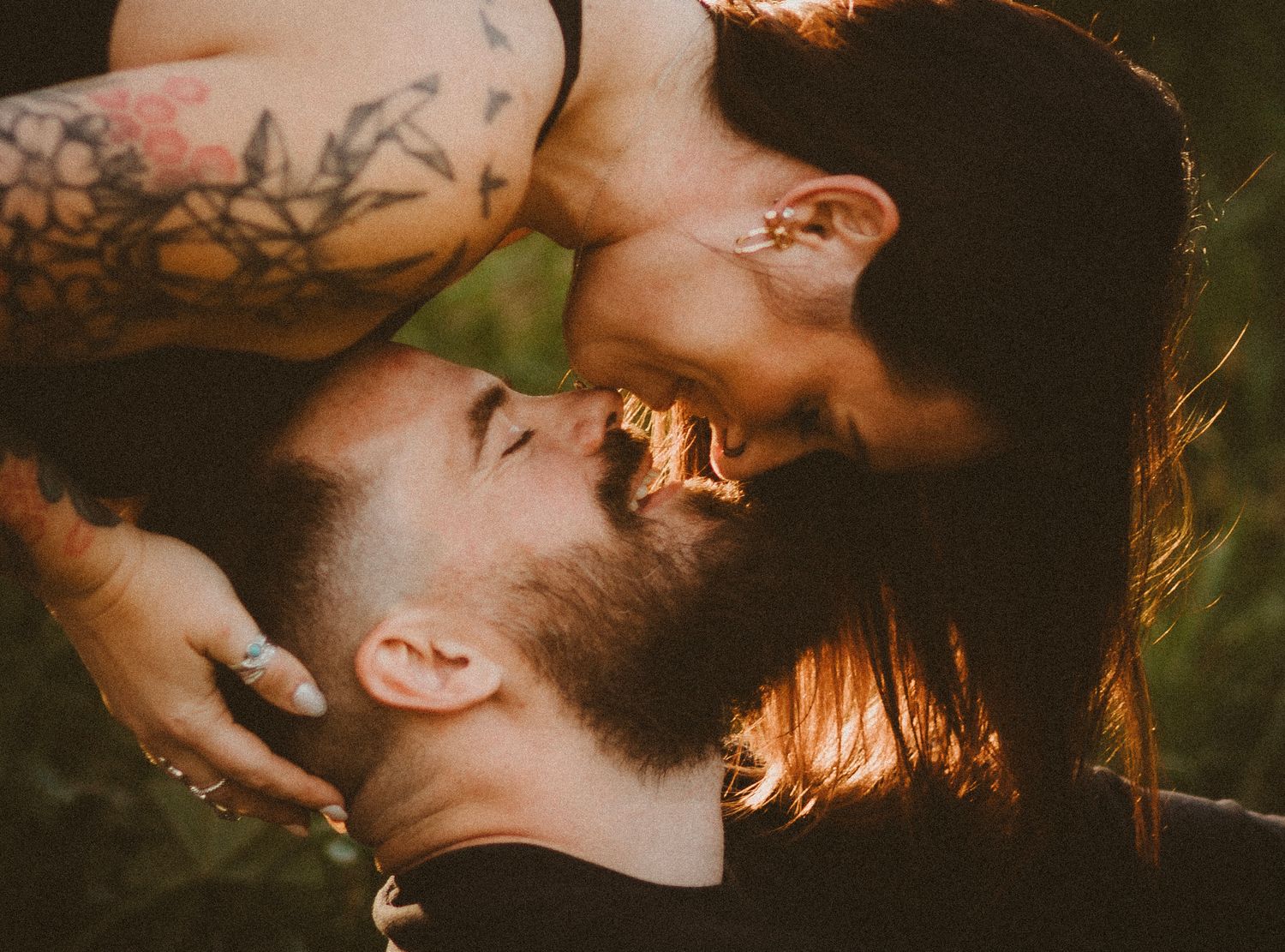 Romantic couple with tattoos sharing an intimate moment outdoors, man with beard and woman with red hair almost kissing.
