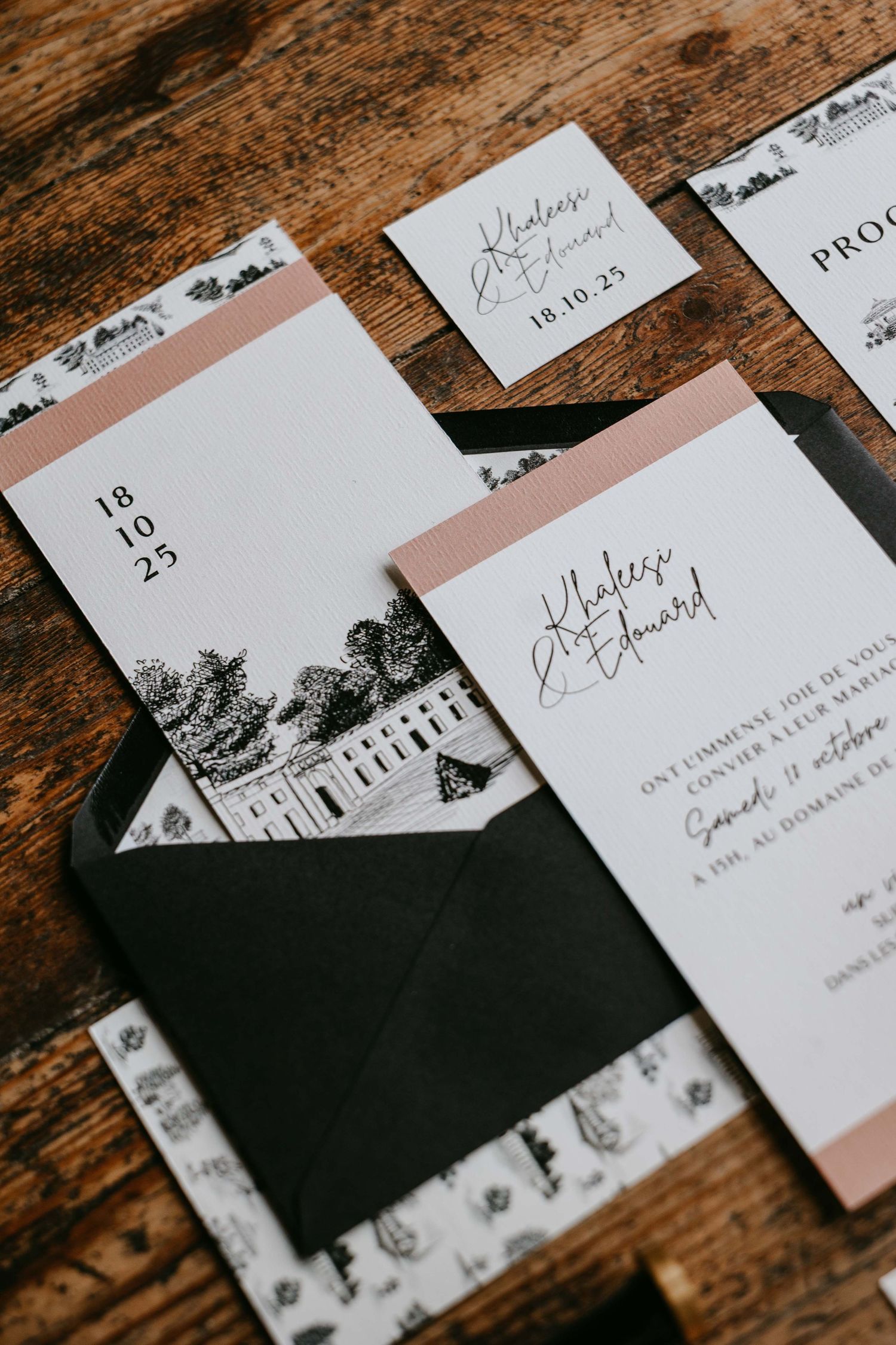 Sophisticated black and white wedding invitation suite with blush pink accents on wood.