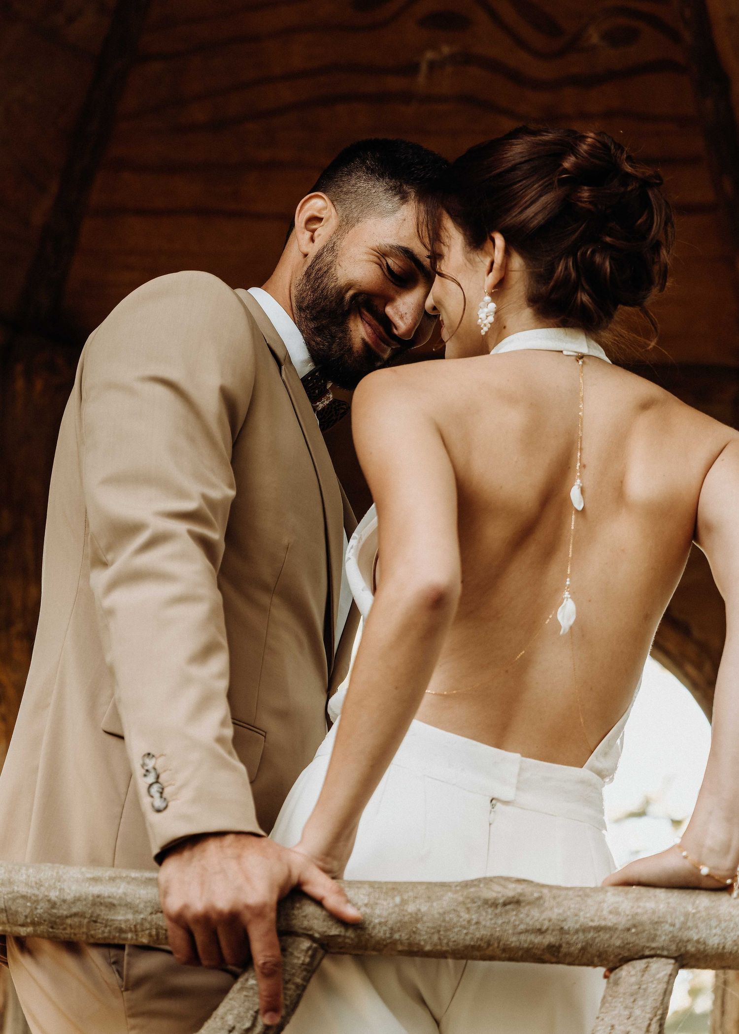 Intimate wedding couple moment, bride in backless white gown with groom in tan suit.