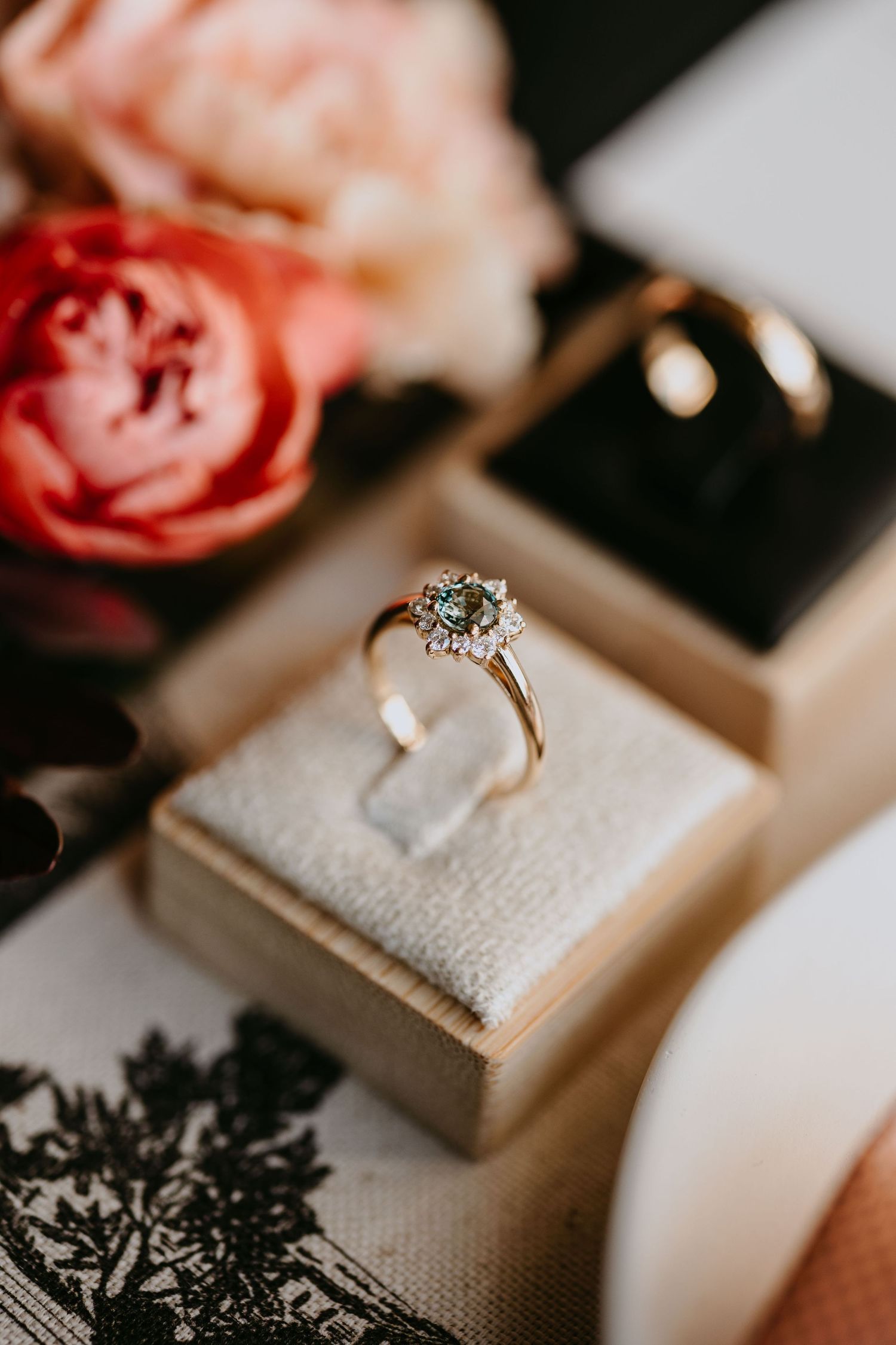 Elegant halo engagement ring with green center stone displayed in a velvet box beside pink roses.