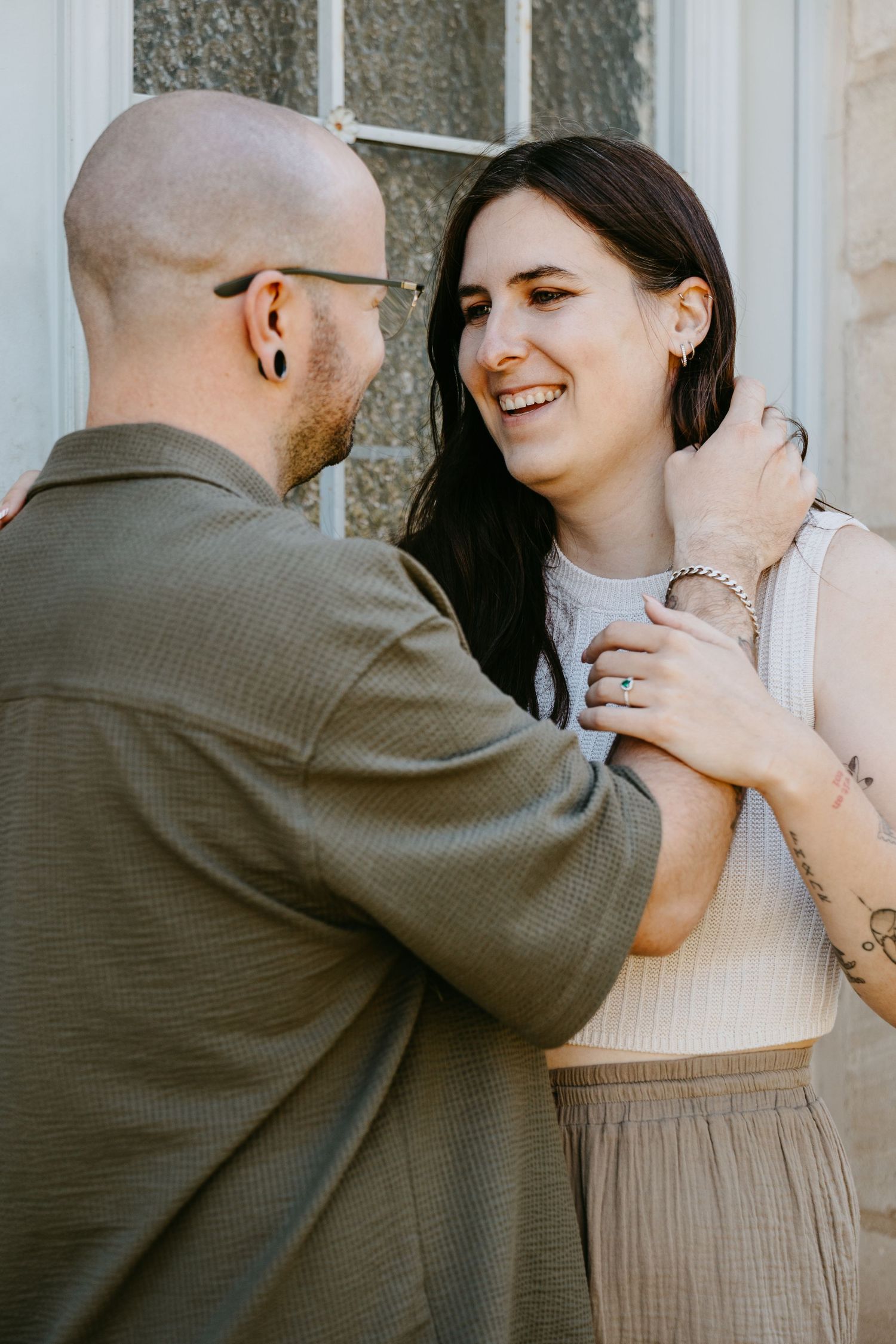 A smiling couple shares a tender moment, the woman laughing joyfully as the man holds her close outdoors.