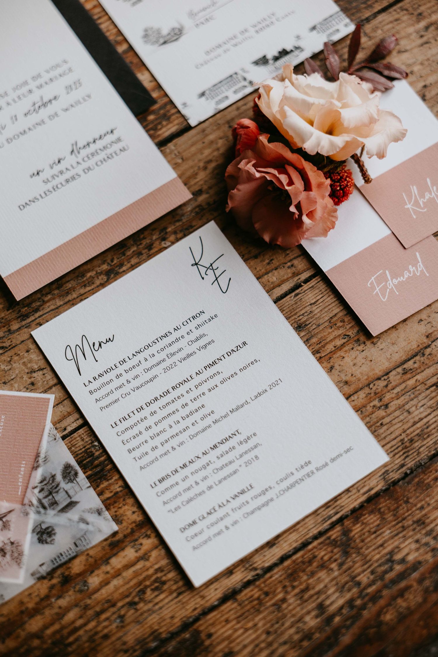 Elegant wedding menu cards with dusty rose accents and floral decoration on rustic wood.