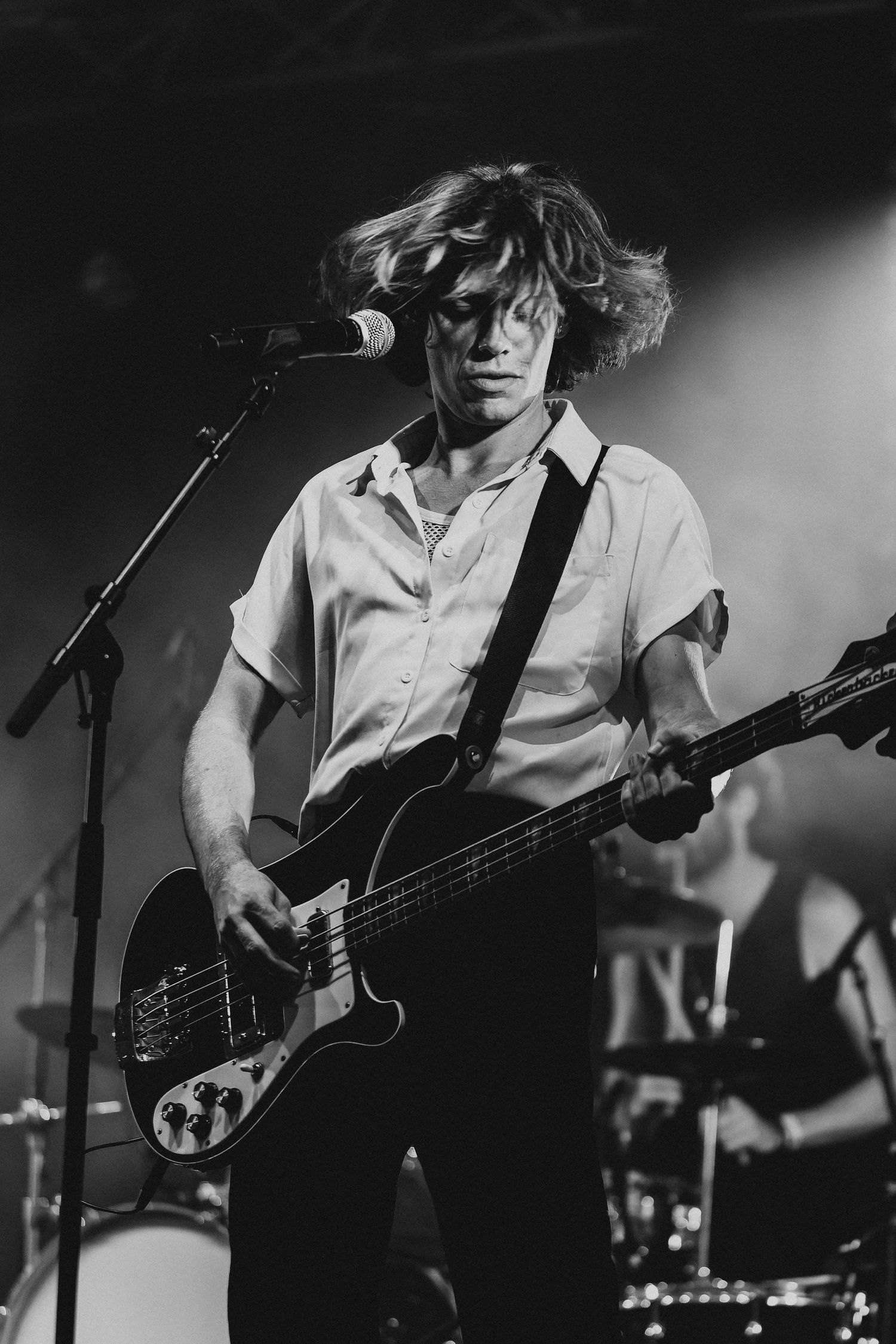 Black and white photo of a guitarist playing bass on stage with flowing hair.