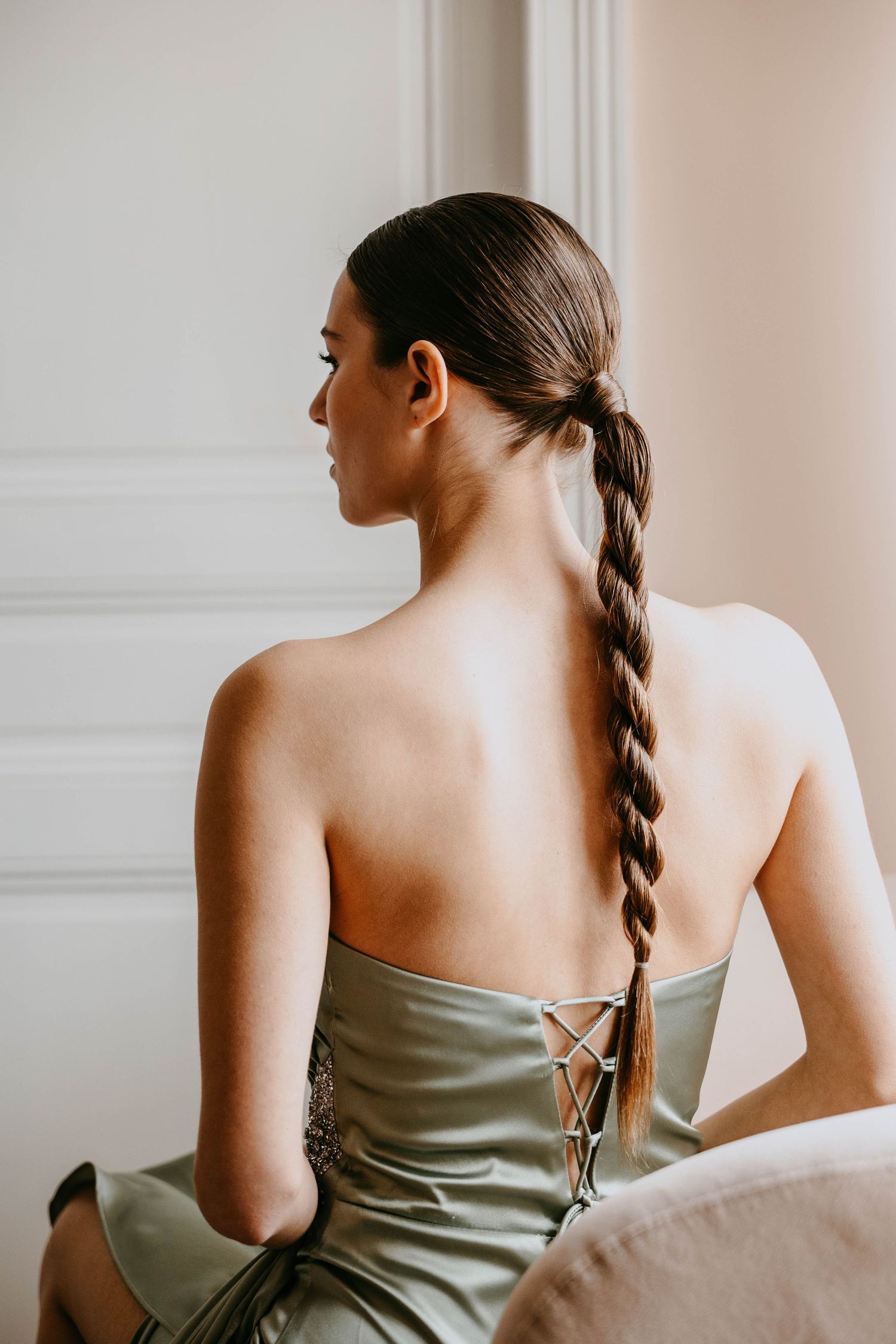 Woman in sage strapless gown with elegant braided ponytail hairstyle, viewed from behind.