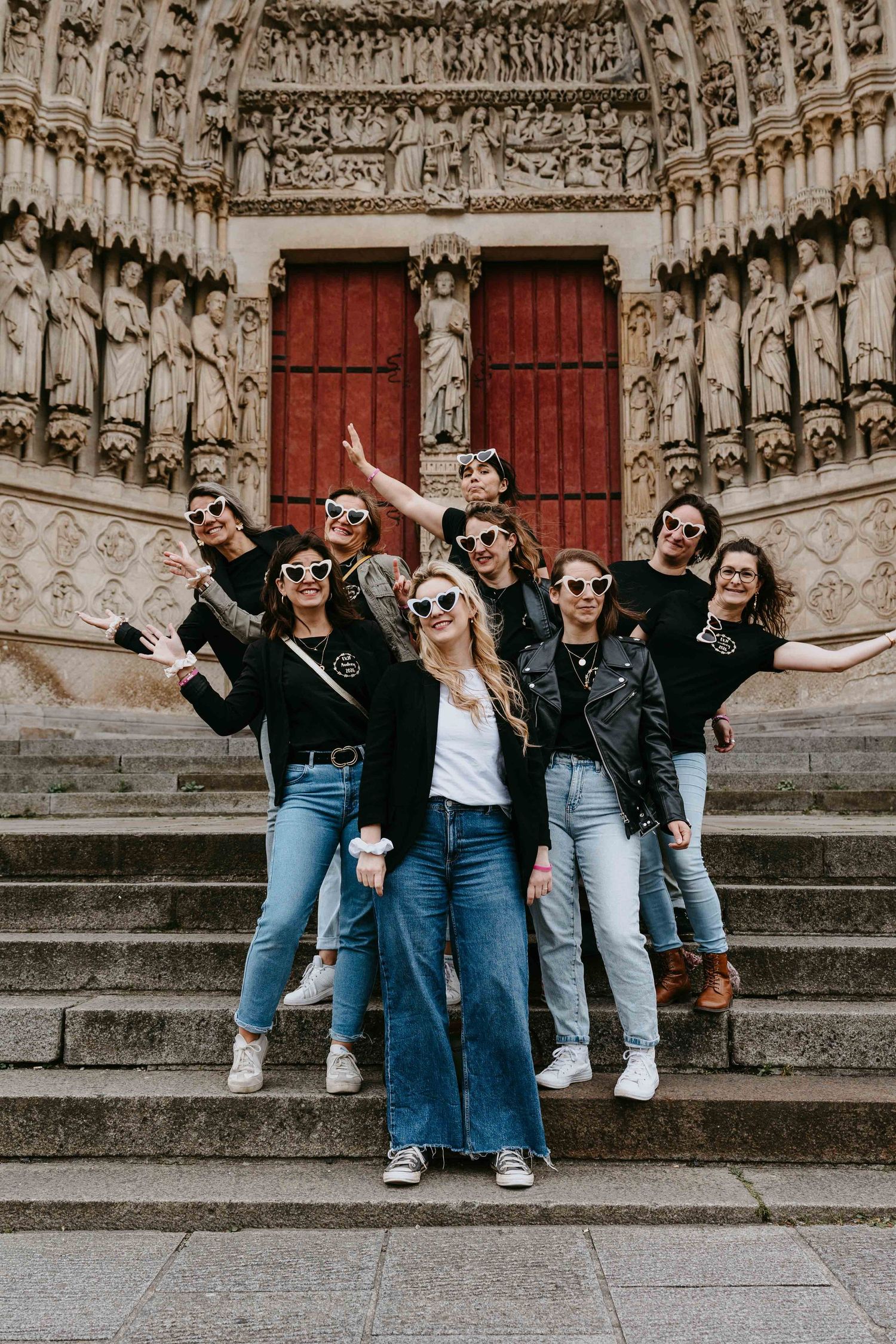 Group of women in black jackets posing on steps in front of ornate cathedral doors.