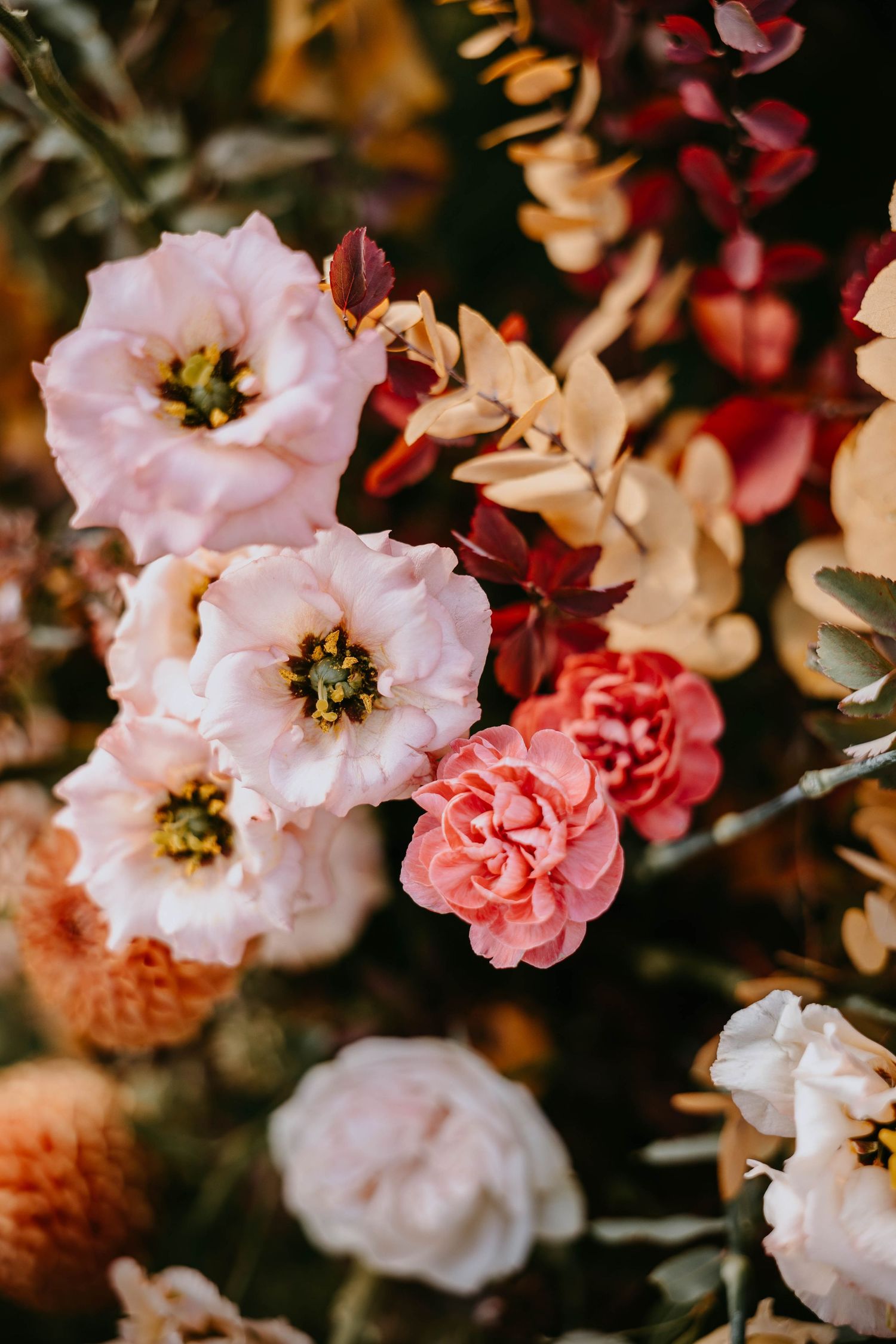Close-up of a beautiful floral arrangement with pink lisianthus, carnations, and autumn foliage.